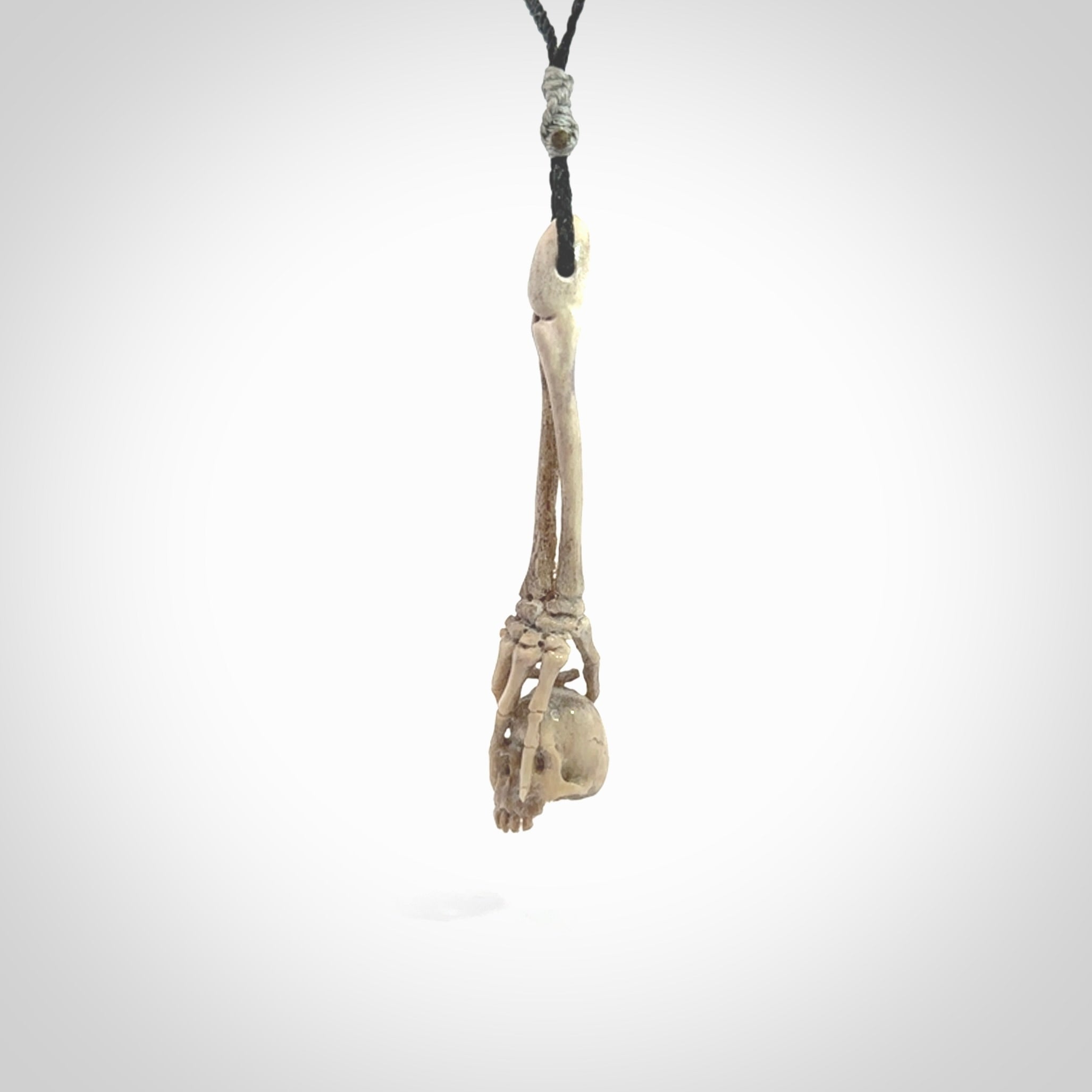 This picture shows a large sized Deer Antler Bone skull in skeleton hand pendant that we have hand carved. It is polished to a soft shine and is a very striking piece. The cord is a black colour and has a small grey floret binding just above the pendant.