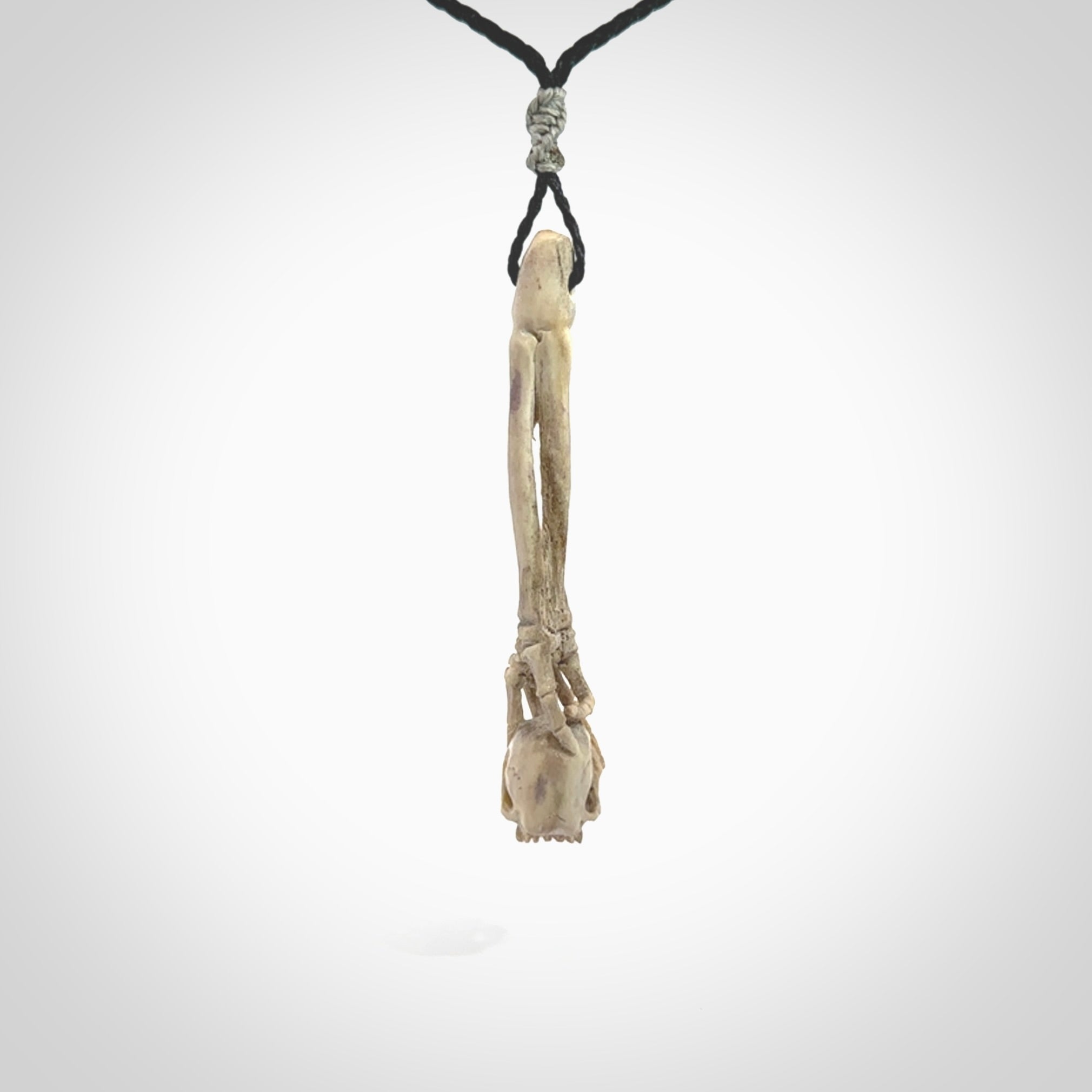 This picture shows a large sized Deer Antler Bone skull in skeleton hand pendant that we have hand carved. It is polished to a soft shine and is a very striking piece. The cord is a black colour and has a small grey floret binding just above the pendant.