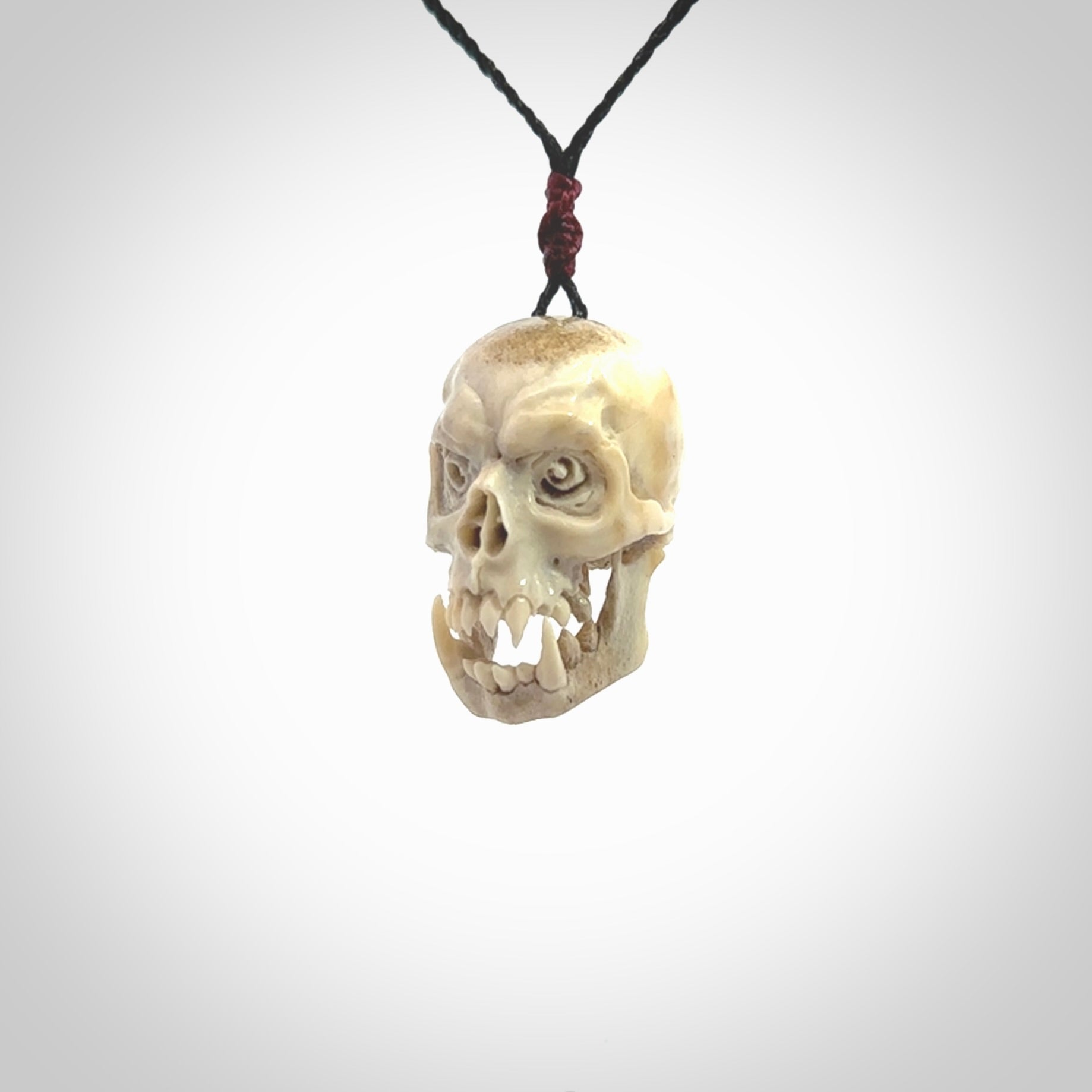 This picture shows a medium sized Deer Antler Bone skull pendant that we have hand carved. It is polished to a soft shine and is a very striking piece. The cord is a black colour and has a small burgundy floret binding just above the pendant.