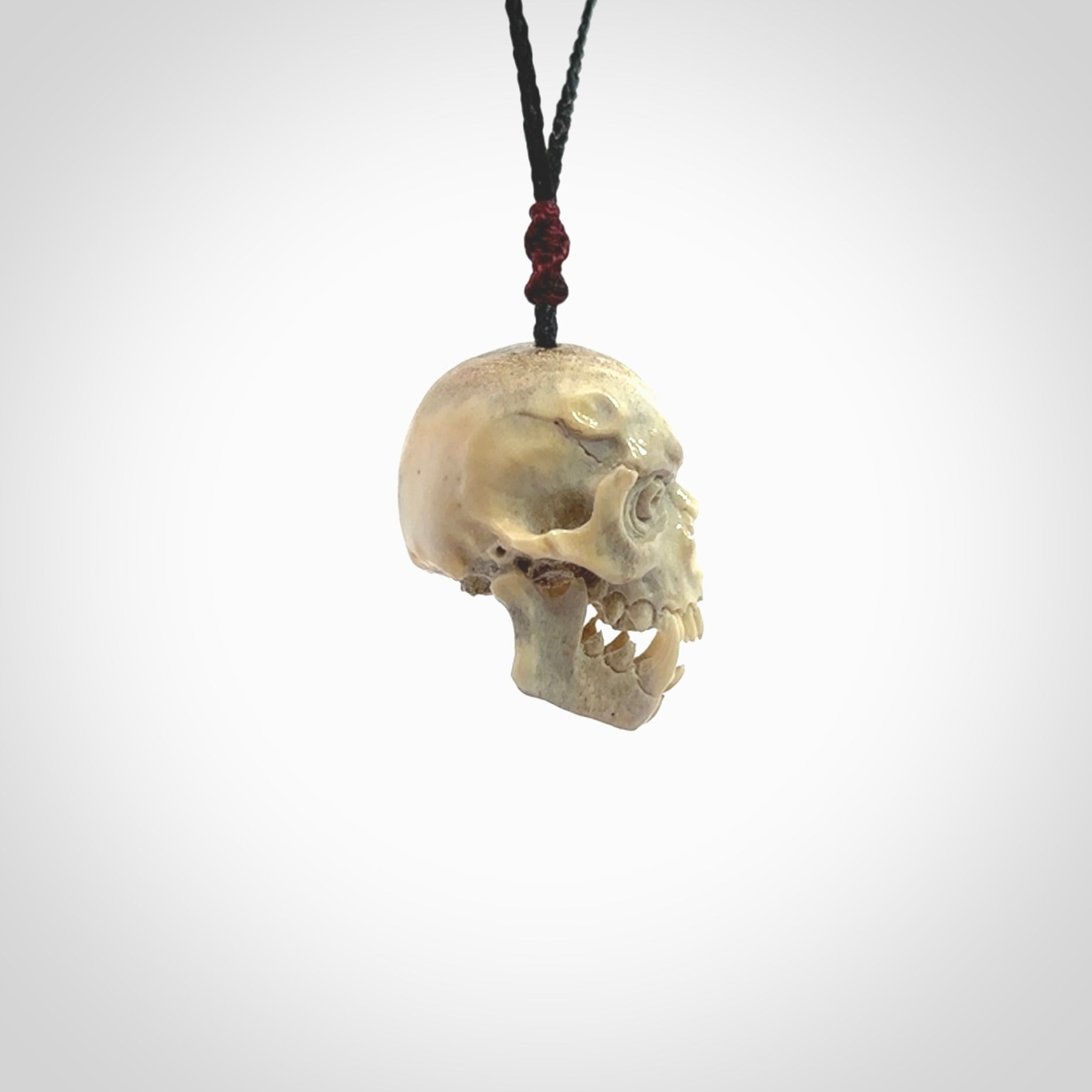 This picture shows a medium sized Deer Antler Bone skull pendant that we have hand carved. It is polished to a soft shine and is a very striking piece. The cord is a black colour and has a small burgundy floret binding just above the pendant.