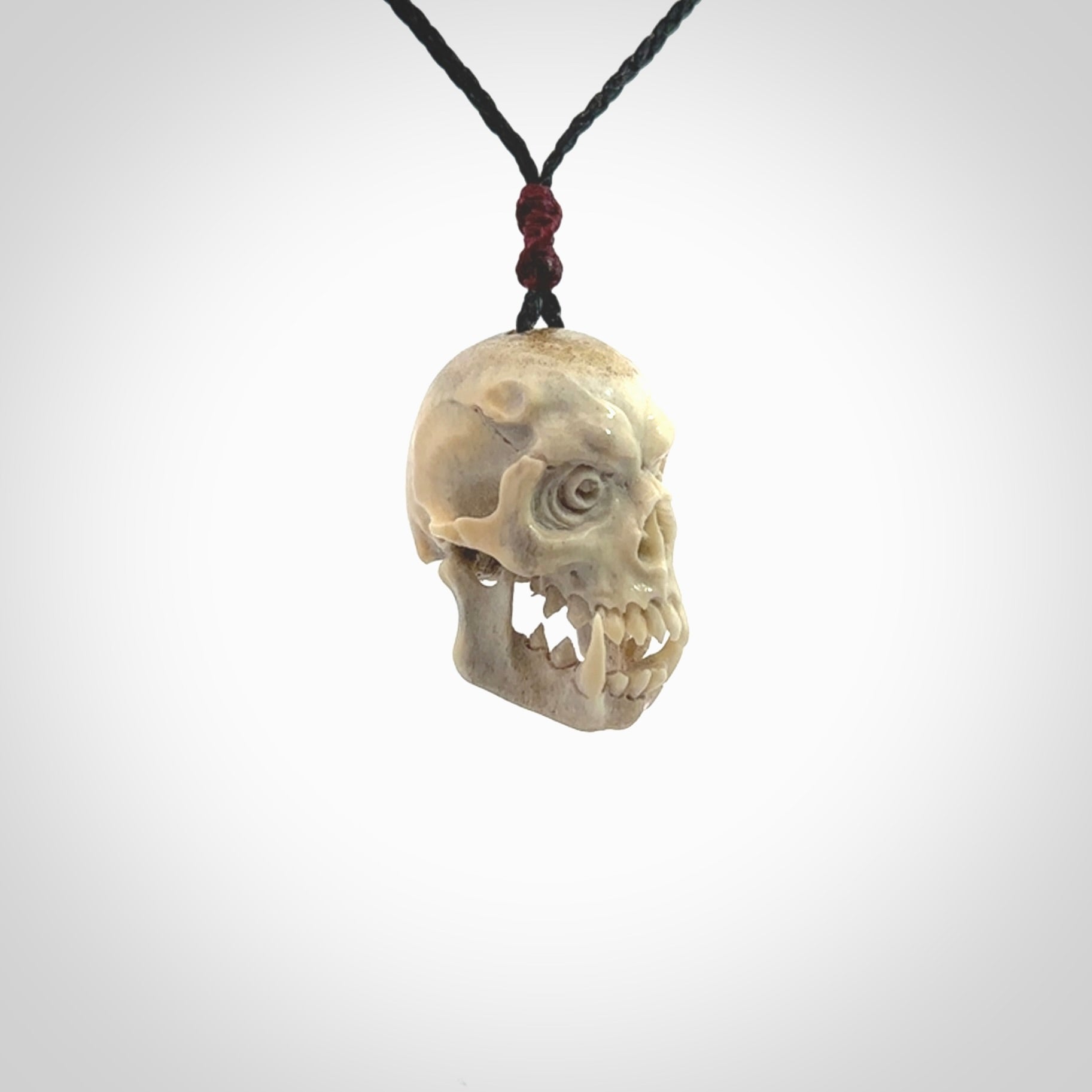 This picture shows a medium sized Deer Antler Bone skull pendant that we have hand carved. It is polished to a soft shine and is a very striking piece. The cord is a black colour and has a small burgundy floret binding just above the pendant.