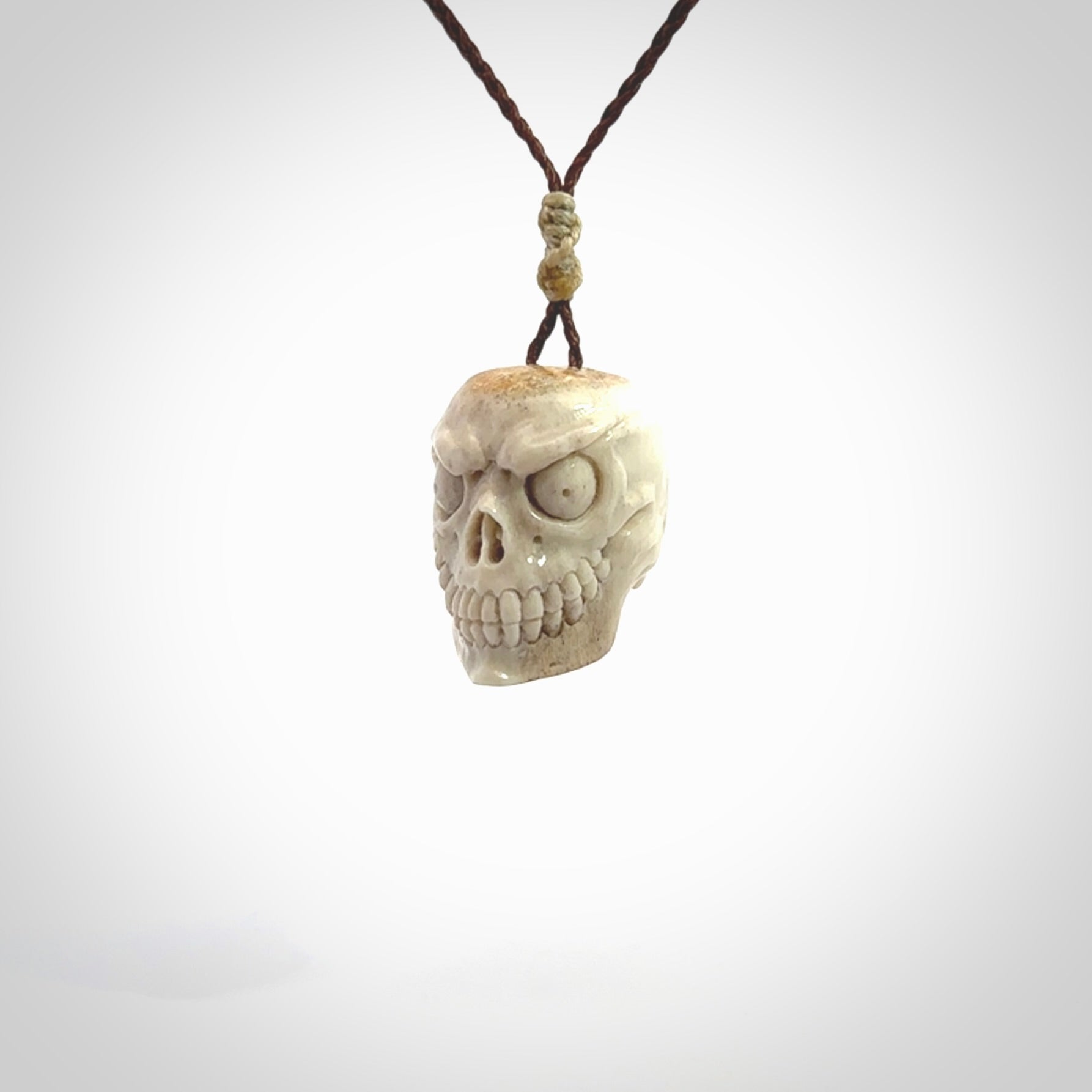 This picture shows a medium sized Deer Antler Bone monster skull pendant that we have hand carved. It is polished to a soft shine and is a very striking piece. The cord is a wapiti brown colour and has a small oat floret binding just above the pendant.