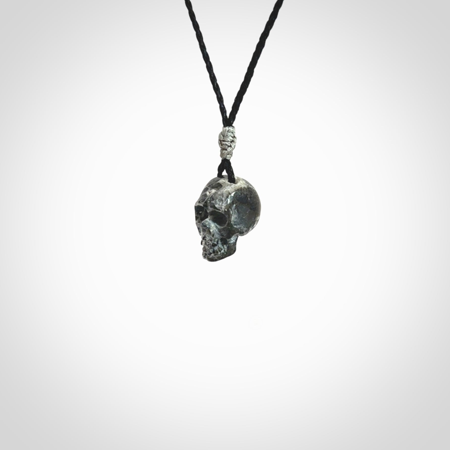 This picture shows a small sized Zebra Marble stone skull pendant that we have hand carved. It is polished to a soft shine and is a very striking piece. The cord is black and has a small grey floret binding just above the pendant.