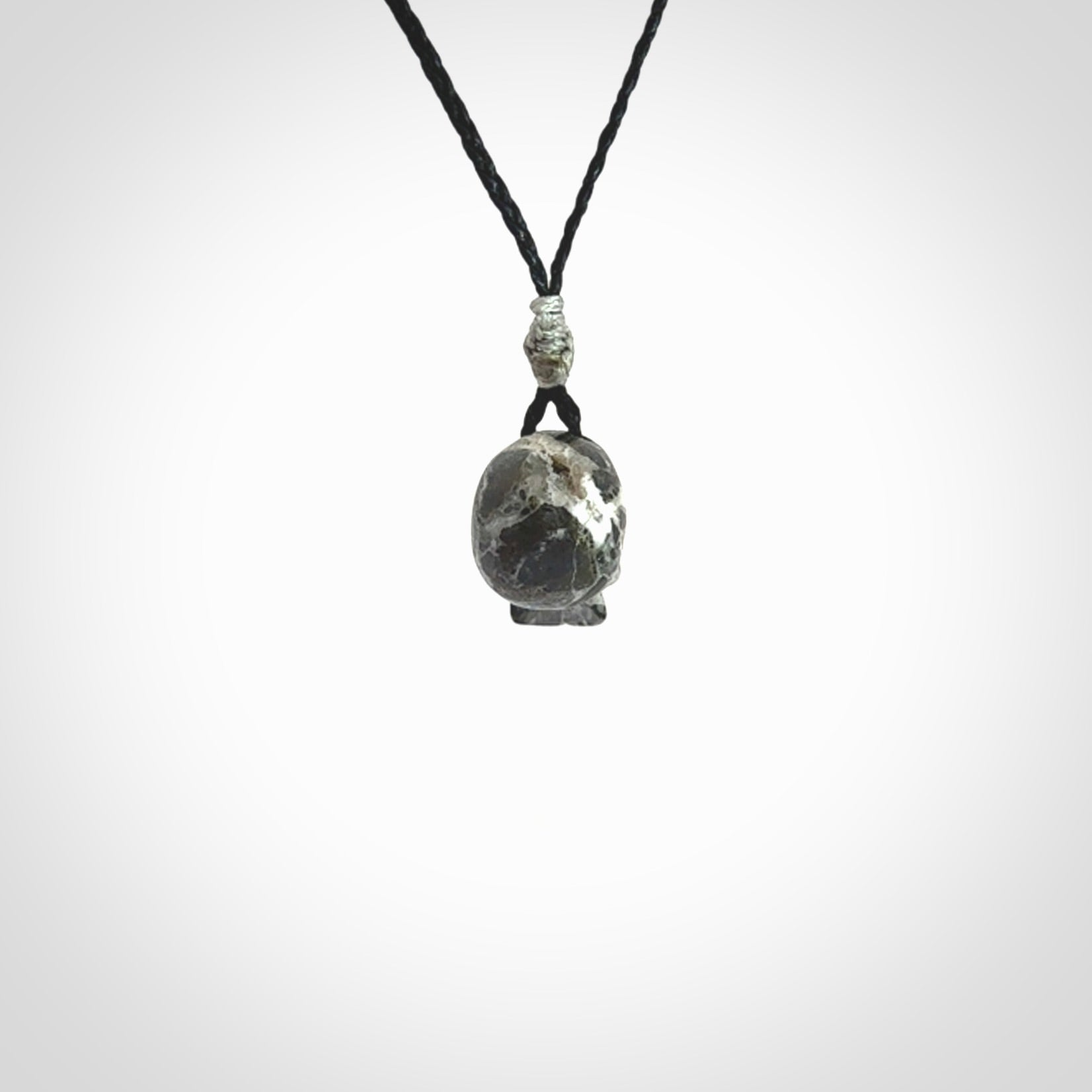 This picture shows a small sized Zebra Marble stone skull pendant that we have hand carved. It is polished to a soft shine and is a very striking piece. The cord is black and has a small grey floret binding just above the pendant.