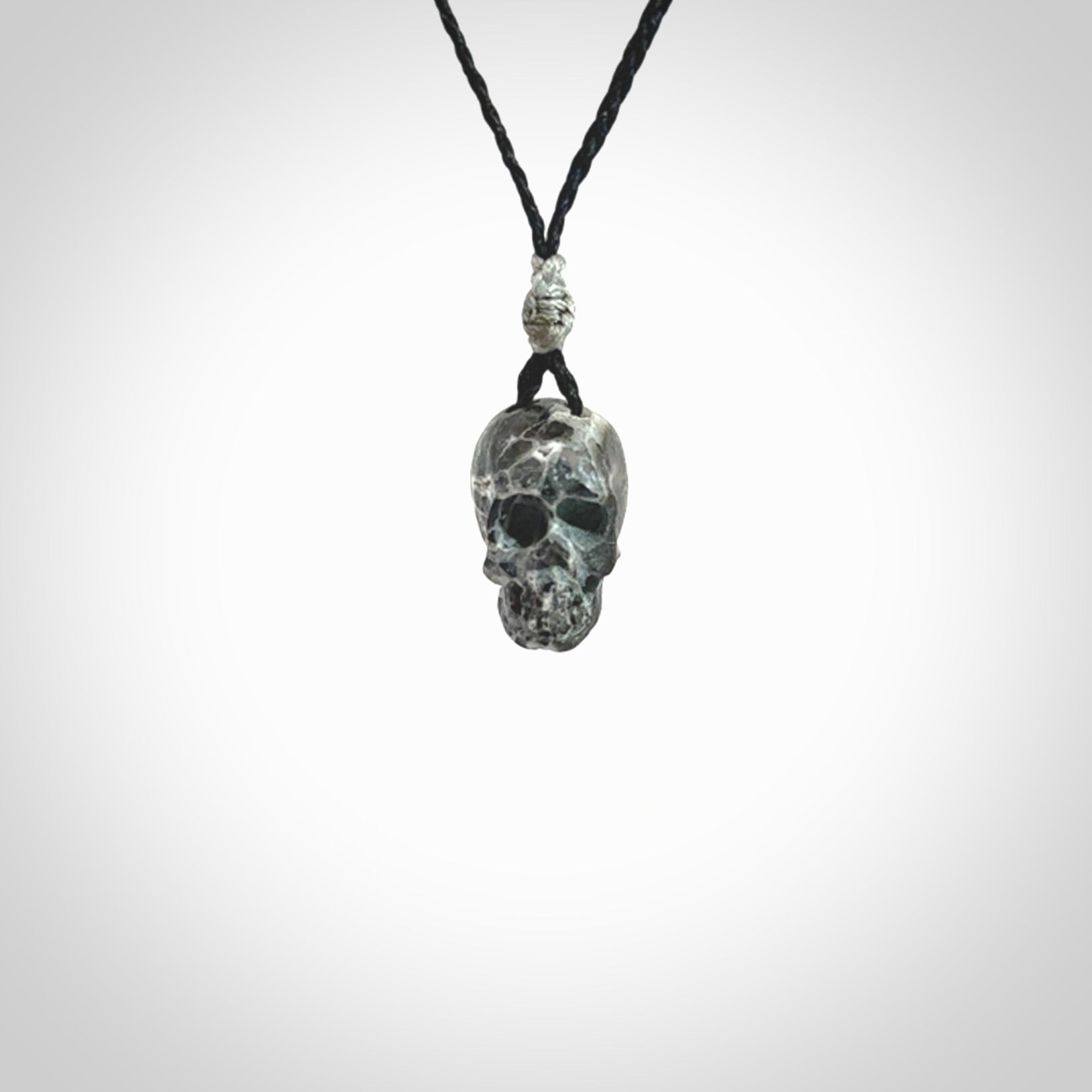 This picture shows a small sized Zebra Marble stone skull pendant that we have hand carved. It is polished to a soft shine and is a very striking piece. The cord is black and has a small grey floret binding just above the pendant.