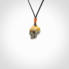 This picture shows a small sized Bumblebee Jasper stone skull pendant that we have hand carved. It is polished to a soft shine and is a very striking piece. The cord is black colour and has a small orange floret binding just above the pendant.