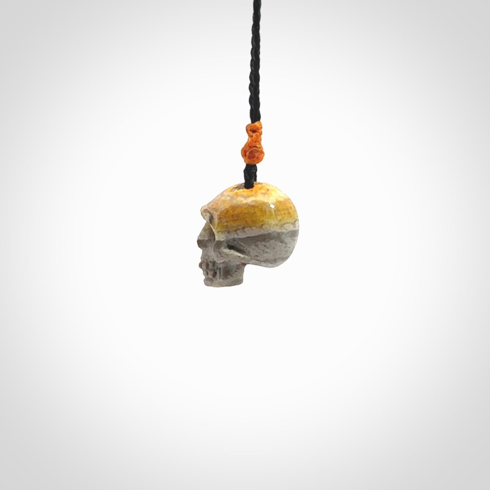 This picture shows a small sized Bumblebee Jasper stone skull pendant that we have hand carved. It is polished to a soft shine and is a very striking piece. The cord is black colour and has a small orange floret binding just above the pendant.