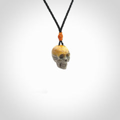 This picture shows a small sized Bumblebee Jasper stone skull pendant that we have hand carved. It is polished to a soft shine and is a very striking piece. The cord is black colour and has a small orange floret binding just above the pendant.