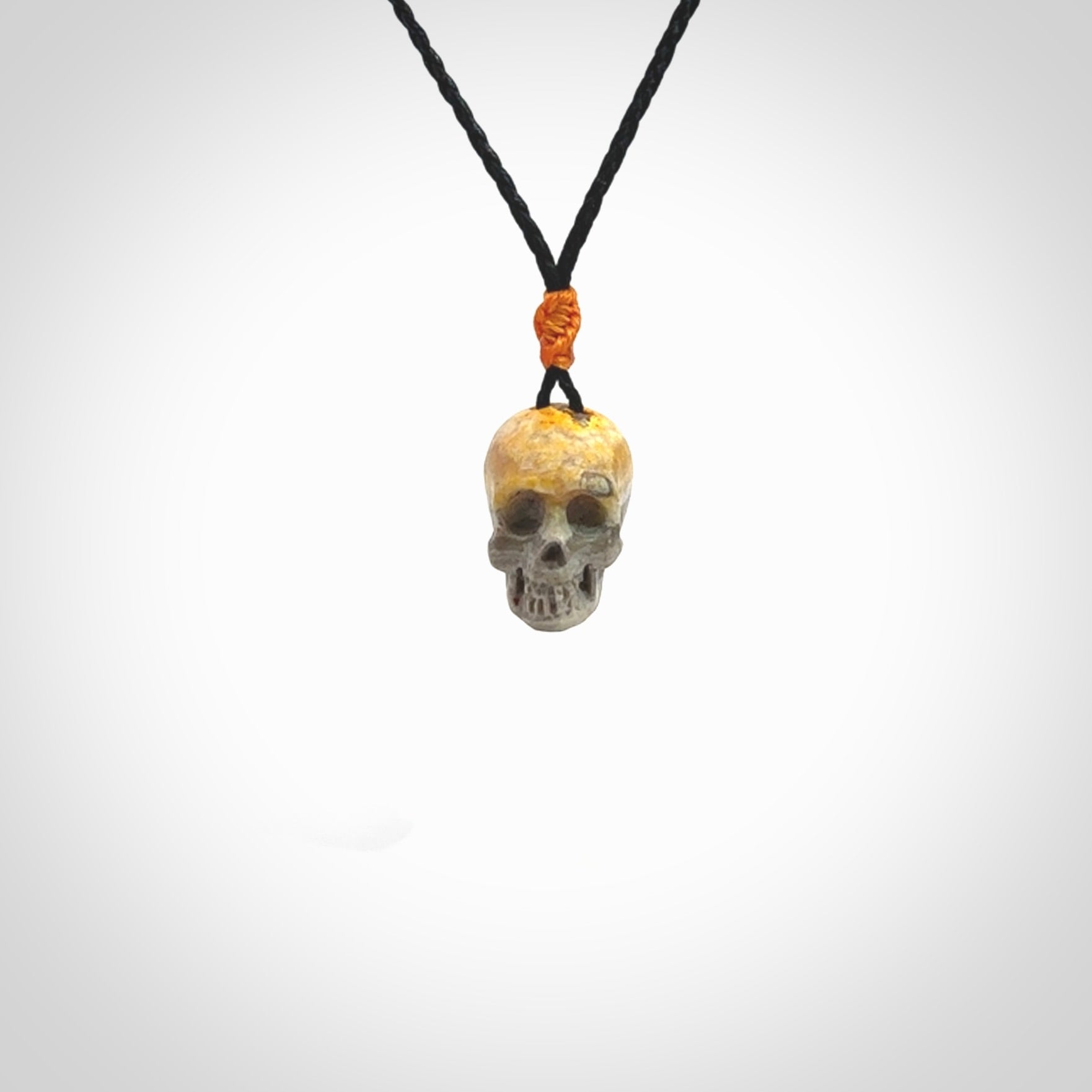 This picture shows a small sized Bumblebee Jasper stone skull pendant that we have hand carved. It is polished to a soft shine and is a very striking piece. The cord is black colour and has a small orange floret binding just above the pendant.