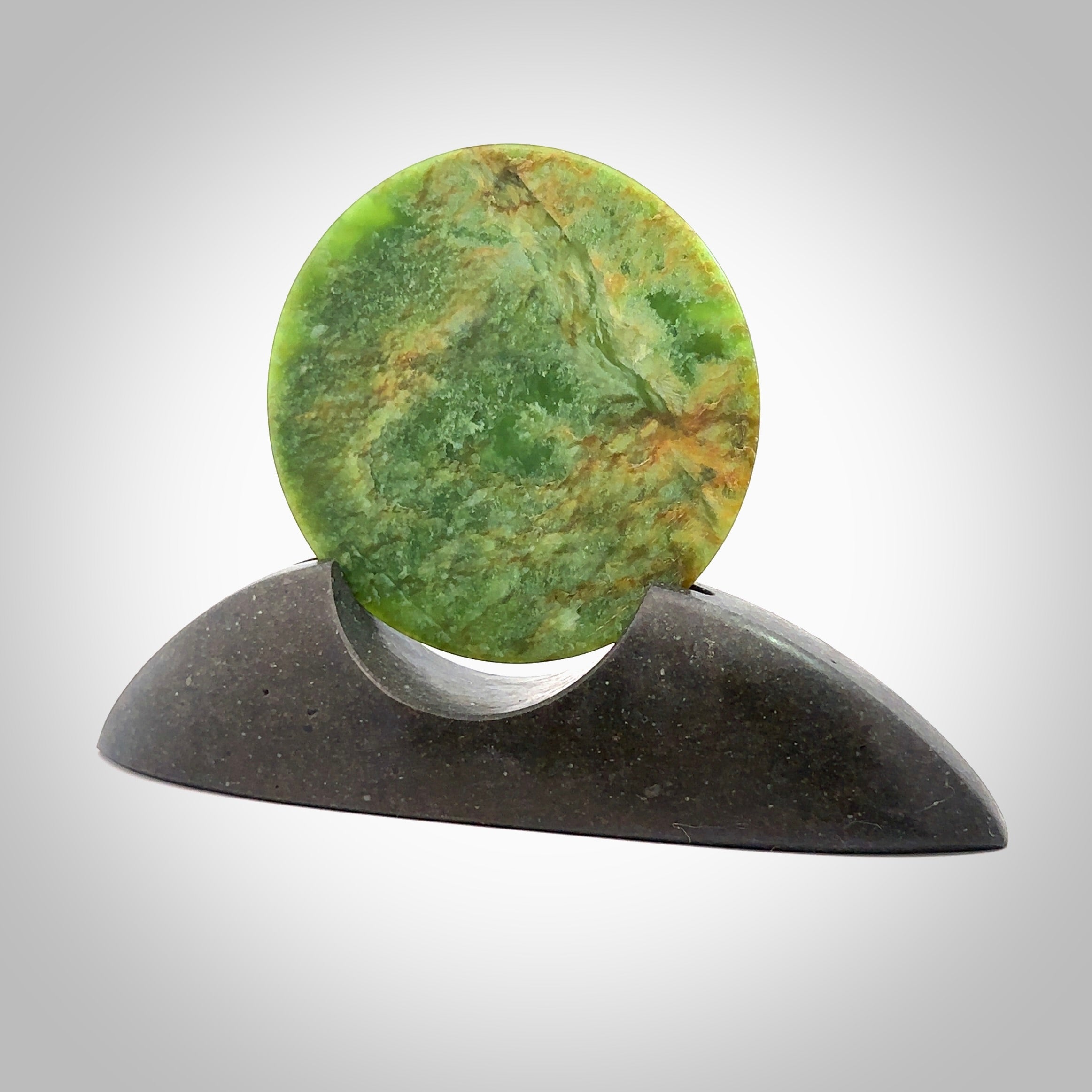 Hand carved New Zealand Flower Jade Disc with Greywacke stand sculpture. Hand carved here in New Zealand by Ric Moor. This is a 'one only' sculpture, a beautiful display piece. Small Jade disc sculpture for desk.