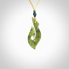 This photo shows a matau pendant carved from New Zealand Jade. The artist, Shaun Gardiner, has carved this beautifully. We provide this piece with an adjustable oat coloured cord. This is a fantastic work of art, we have one only.