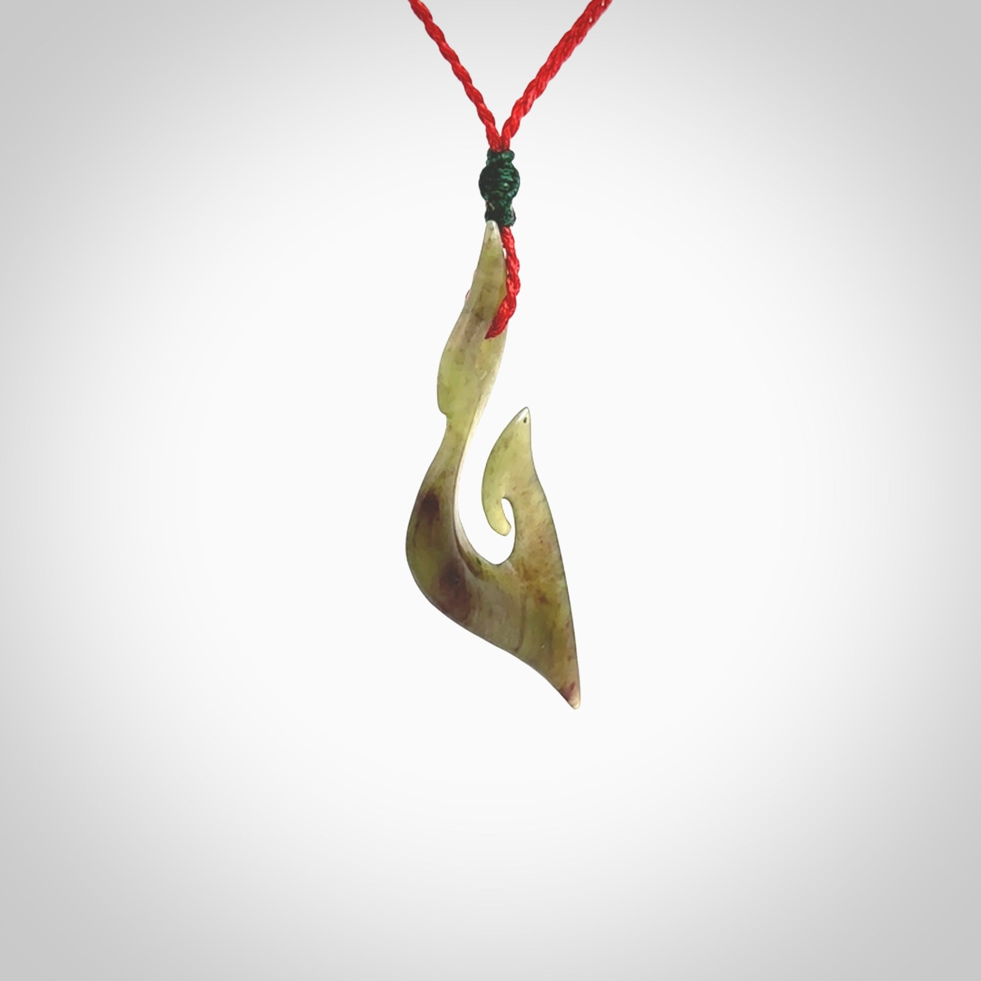 This photo shows a matau pendant carved from New Zealand Totoweka Pounamu, Jade. The artist, Shaun Gardiner, has carved this beautifully. We provide this piece with an adjustable red coloured cord. This is a fantastic work of art, we have one only.