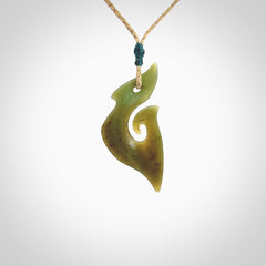 This photo shows a matau pendant carved from New Zealand Totoweka Pounamu, Jade. The artist, Shaun Gardiner, has carved this beautifully. We provide this piece with an adjustable tan coloured cord. This is a fantastic work of art, we have one only.