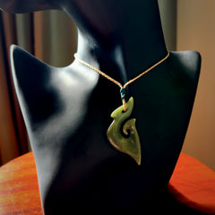 This photo shows a matau pendant carved from New Zealand Totoweka Pounamu, Jade. The artist, Shaun Gardiner, has carved this beautifully. We provide this piece with an adjustable tan coloured cord. This is a fantastic work of art, we have one only.