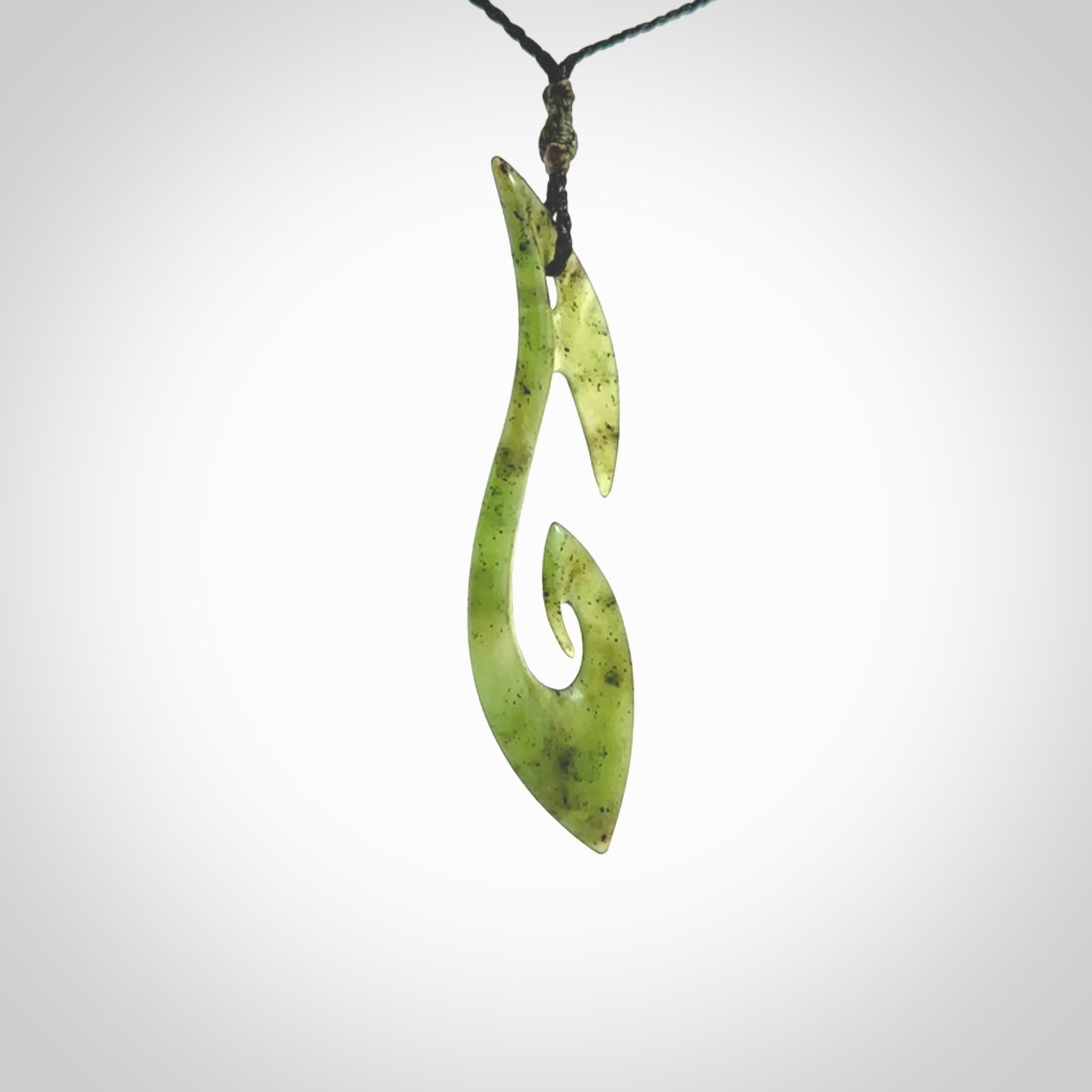 This photo shows a large contemporary matau pendant carved from New Zealand Jade. The artist, Shaun Gardiner, has carved this beautifully. We provide this piece with an adjustable black coloured cord. This is a fantastic work of art, we have one only.