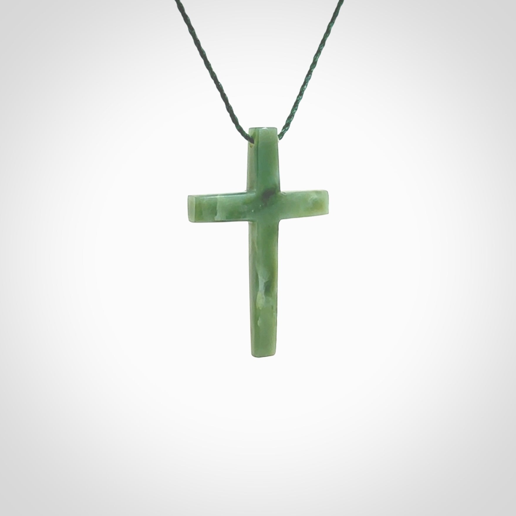 Hand carved jade cross. Made from New Zealand jade. Christian cross for sale online.This picture shows a green jade cross suspended on a fine, plaited cord. The cross is hand carved jade cross. Made from New Zealand jade. Christian cross for sale online.