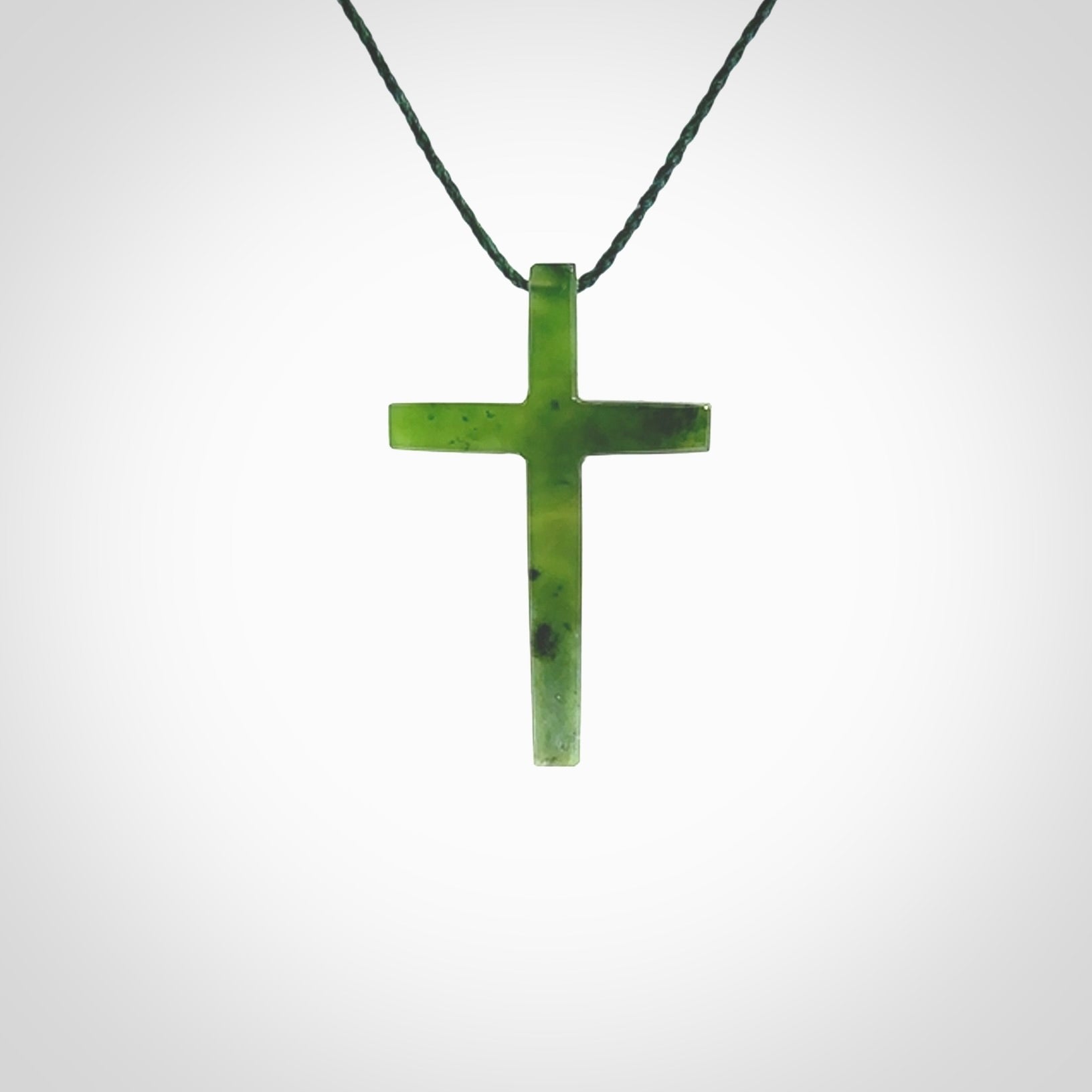 Hand carved jade cross. Made from New Zealand jade. Christian cross for sale online.This picture shows a green jade cross suspended on a fine, plaited cord. The cross is hand carved jade cross. Made from New Zealand jade. Christian cross for sale online.