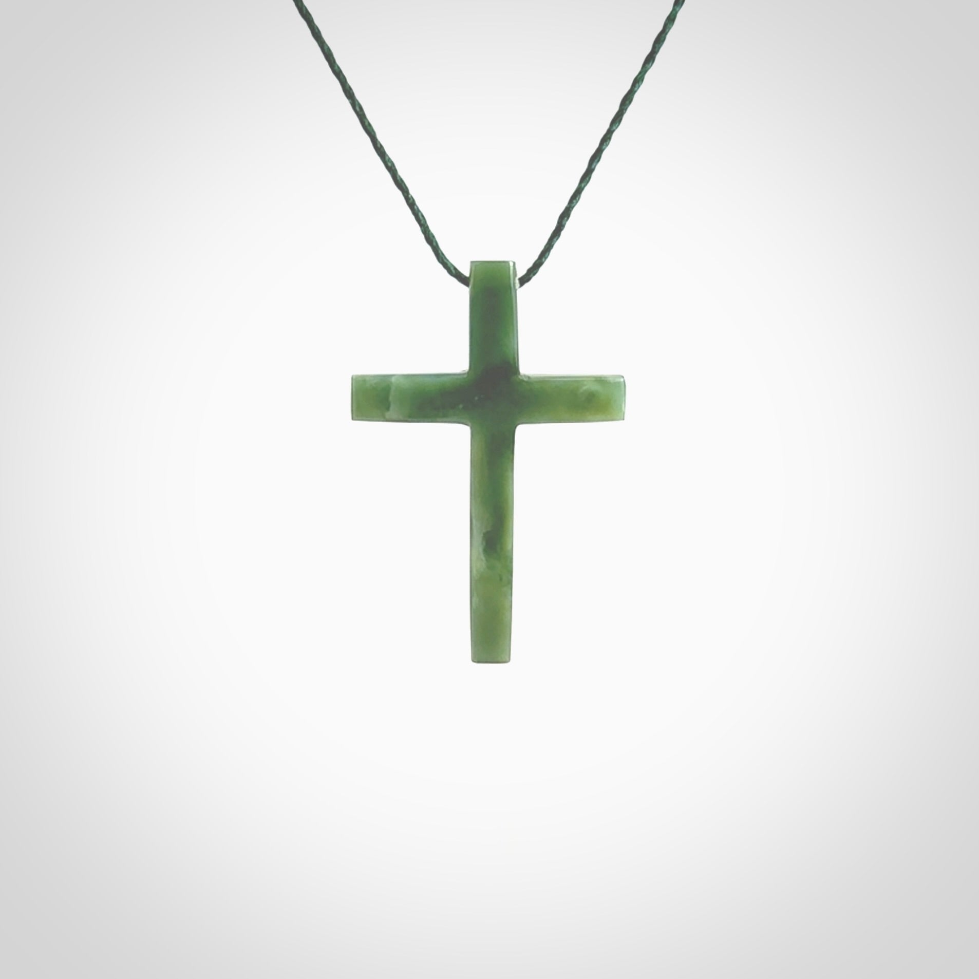 Hand carved jade cross. Made from New Zealand jade. Christian cross for sale online.This picture shows a green jade cross suspended on a fine, plaited cord. The cross is hand carved jade cross. Made from New Zealand jade. Christian cross for sale online.