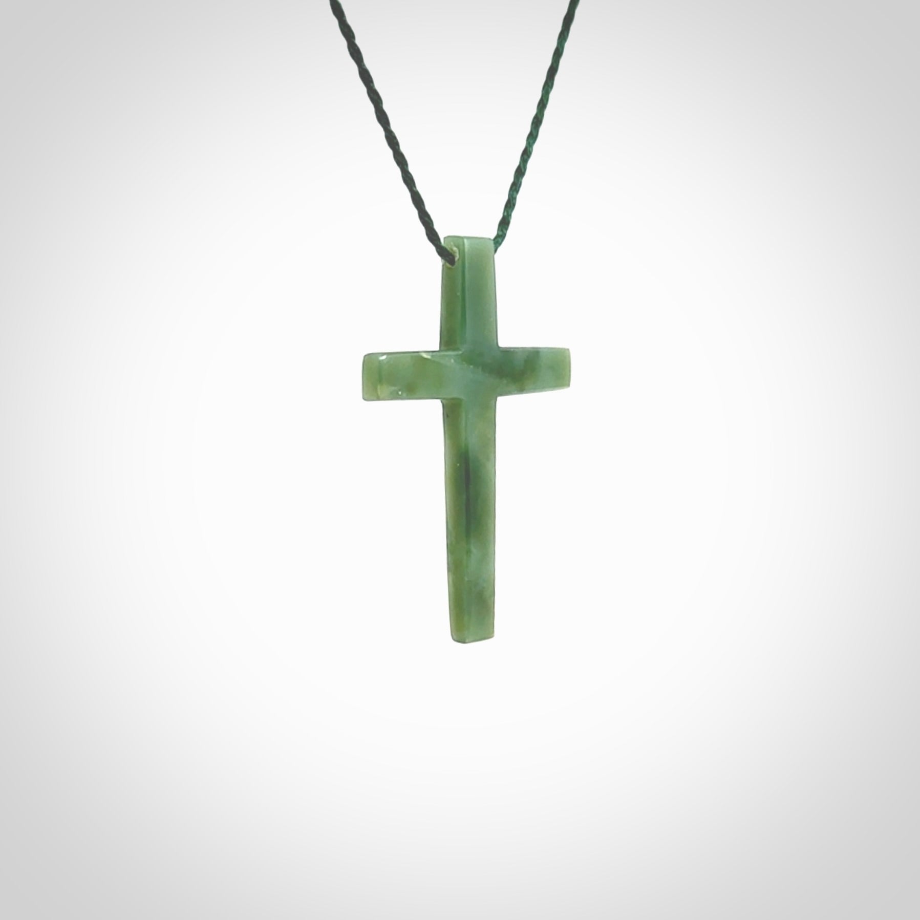 Hand carved jade cross. Made from New Zealand jade. Christian cross for sale online.This picture shows a green jade cross suspended on a fine, plaited cord. The cross is hand carved jade cross. Made from New Zealand jade. Christian cross for sale online.