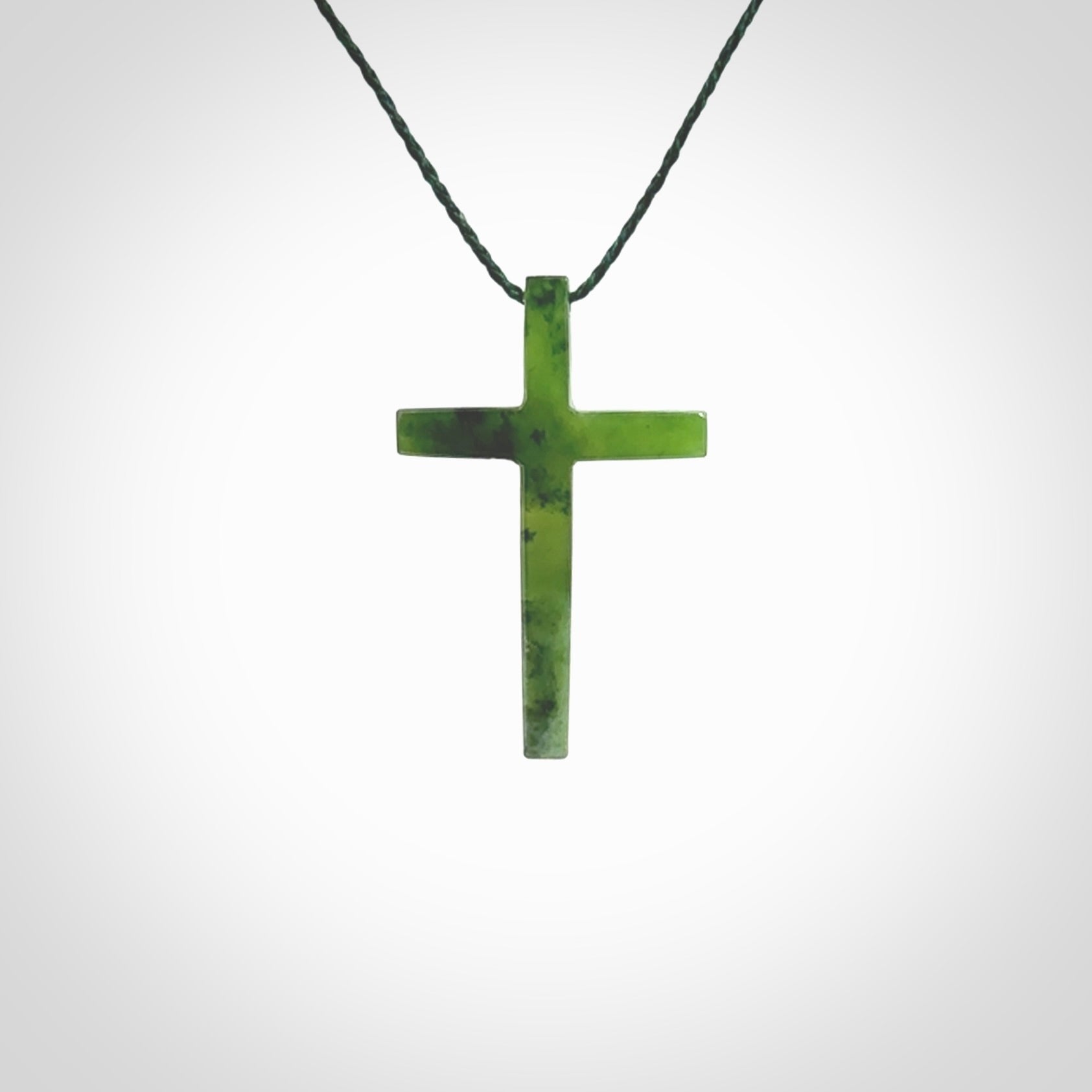 Hand carved jade cross. Made from New Zealand jade. Christian cross for sale online.This picture shows a green jade cross suspended on a fine, plaited cord. The cross is hand carved jade cross. Made from New Zealand jade. Christian cross for sale online.