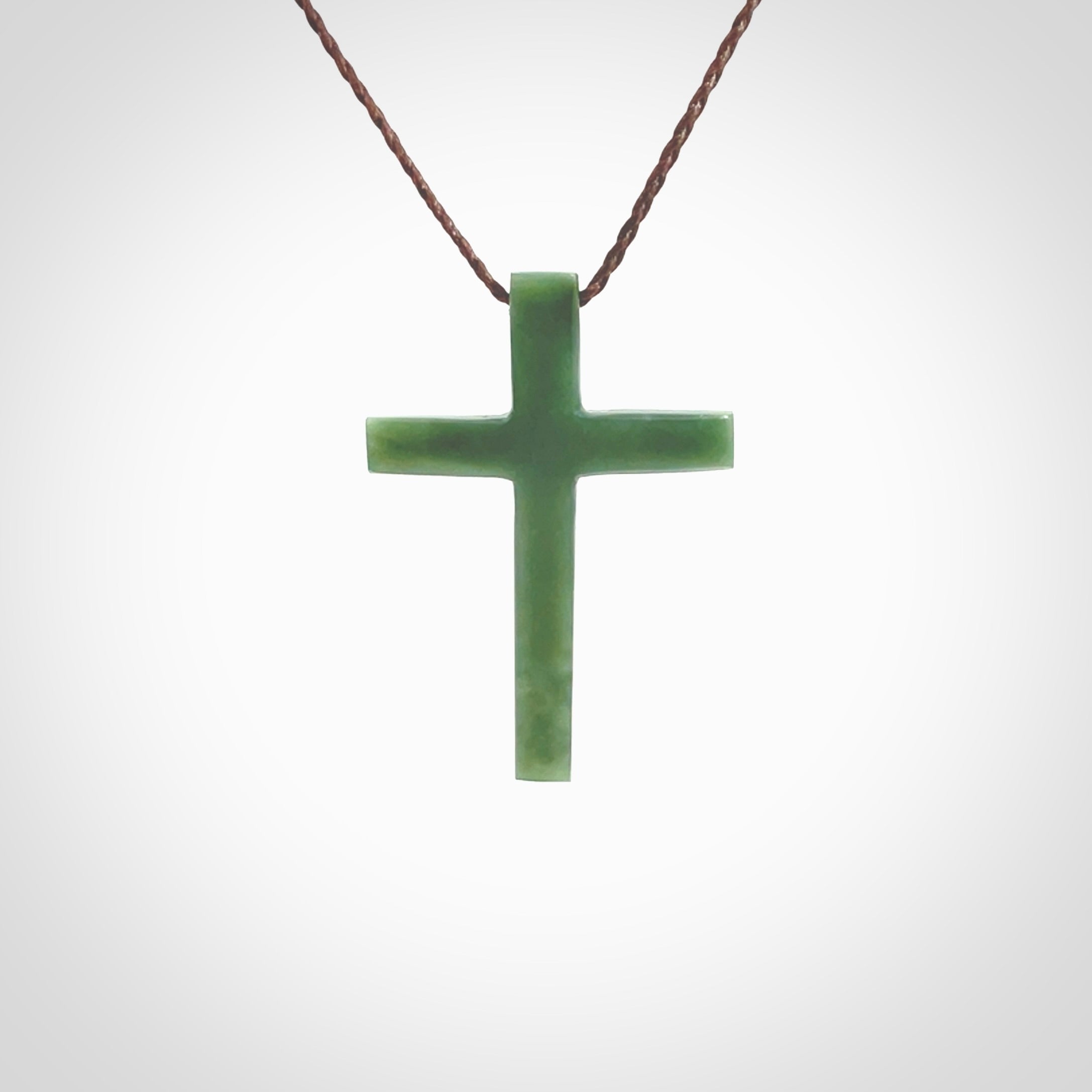 Hand carved jade cross. Made from New Zealand jade. Christian cross for sale online.This picture shows a green jade cross suspended on a fine, plaited cord. The cross is hand carved jade cross. Made from New Zealand jade. Christian cross for sale online.