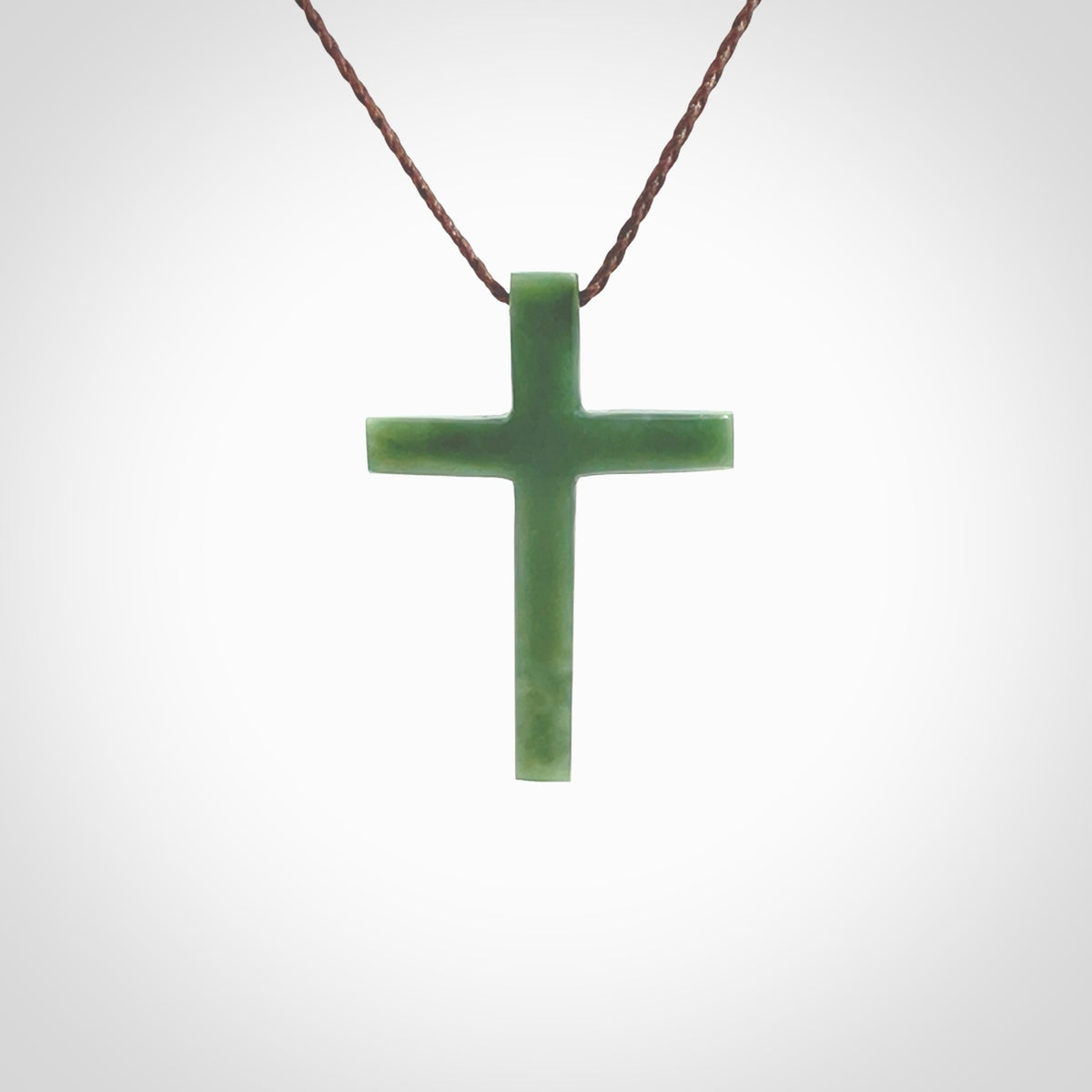 Hand carved jade cross. Made from New Zealand jade. Christian cross for sale online.This picture shows a green jade cross suspended on a fine, plaited cord. The cross is hand carved jade cross. Made from New Zealand jade. Christian cross for sale online.