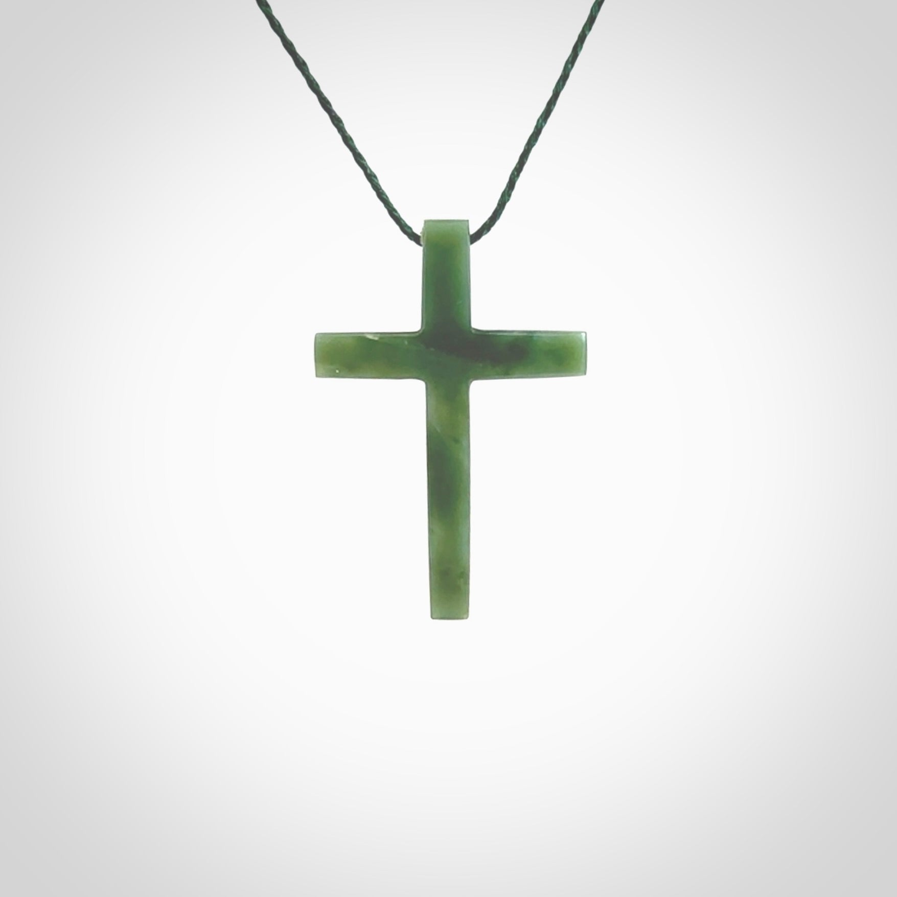 Hand carved jade cross. Made from New Zealand jade. Christian cross for sale online.This picture shows a green jade cross suspended on a fine, plaited cord. The cross is hand carved jade cross. Made from New Zealand jade. Christian cross for sale online.