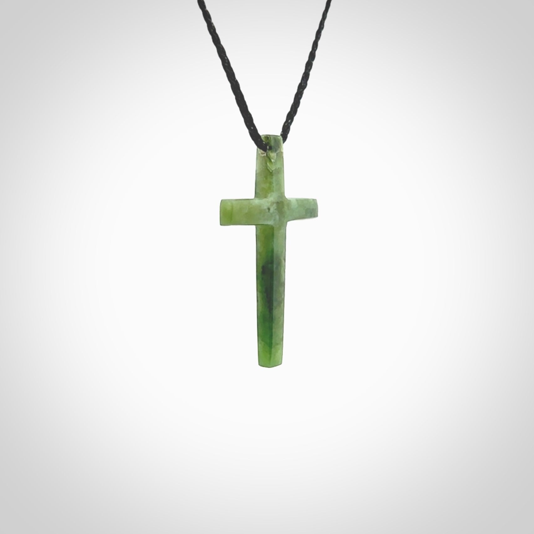 Hand carved jade cross. Made from New Zealand jade. Christian cross for sale online.This picture shows a green jade cross suspended on a fine, plaited cord. The cross is hand carved jade cross. Made from New Zealand jade. Christian cross for sale online.