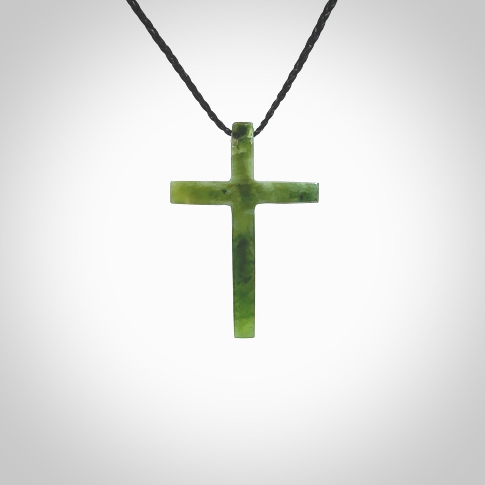 Hand carved jade cross. Made from New Zealand jade. Christian cross for sale online.This picture shows a green jade cross suspended on a fine, plaited cord. The cross is hand carved jade cross. Made from New Zealand jade. Christian cross for sale online.