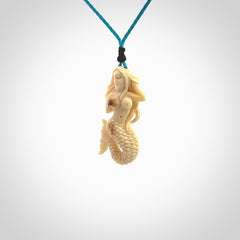 This photo shows a photo of a mermaid pendant. It is handcarved from a beautifully creamy piece of woolly mammoth tusk. It is suspended on an adjustable cord.