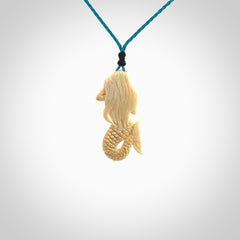 This photo shows a photo of a mermaid pendant. It is handcarved from a beautifully creamy piece of woolly mammoth tusk. It is suspended on an adjustable cord.