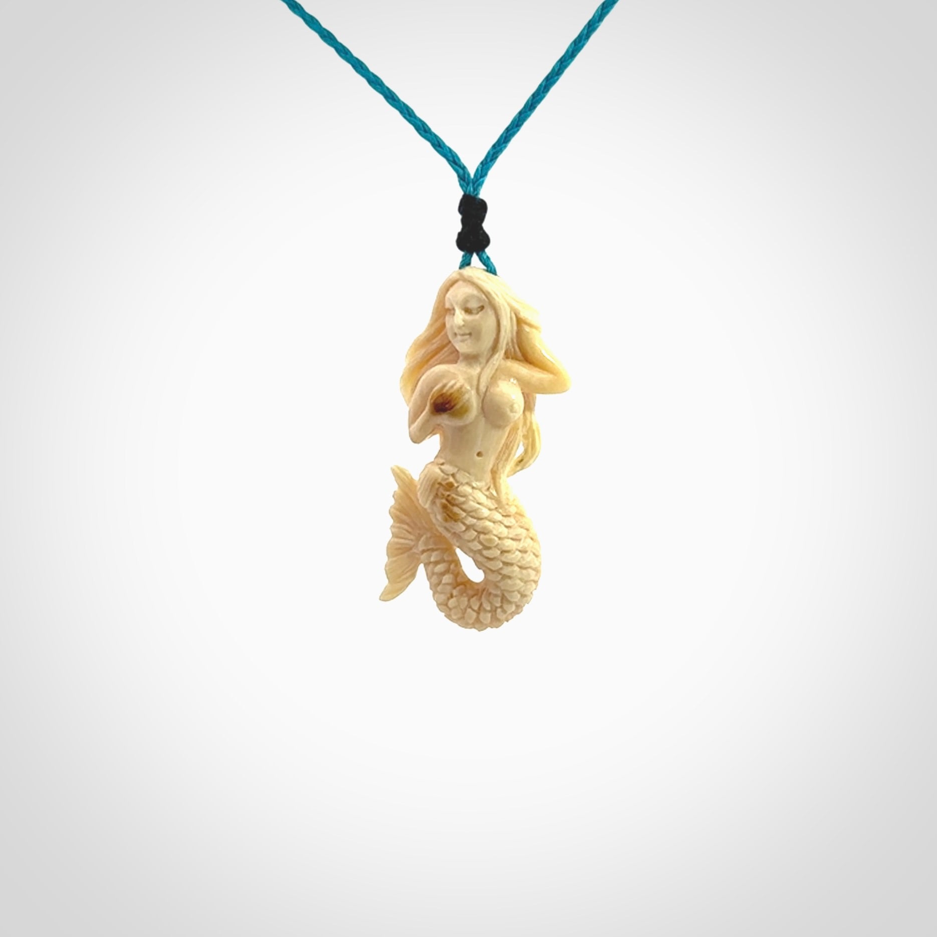 This photo shows a photo of a mermaid pendant. It is handcarved from a beautifully creamy piece of woolly mammoth tusk. It is suspended on an adjustable cord.