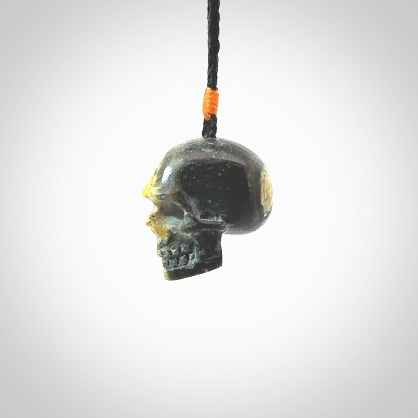 This picture shows a medium sized Bumblebee Jasper stone skull pendant that we have hand carved. It is polished to a soft shine and is a very striking piece. The cord is black colour and has a small orange popper binding just above the pendant.