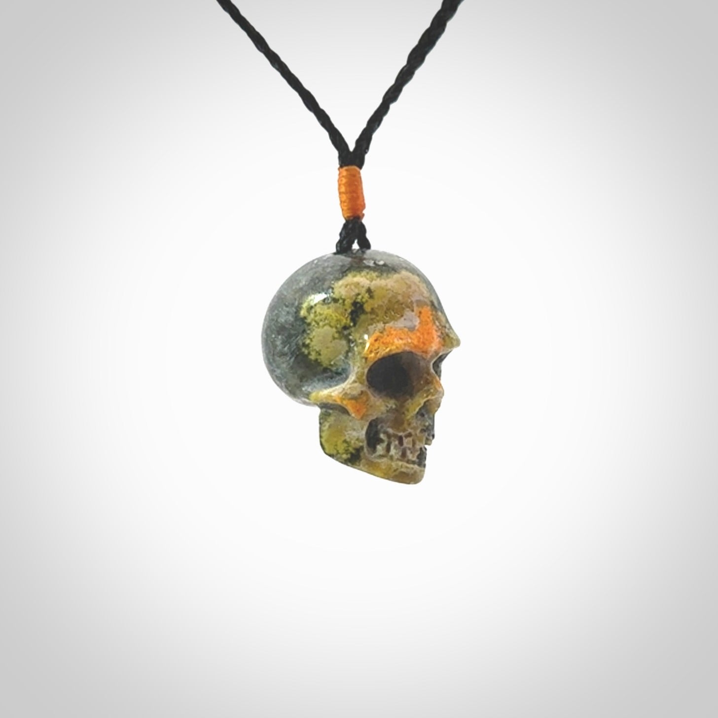 This picture shows a medium sized Bumblebee Jasper stone skull pendant that we have hand carved. It is polished to a soft shine and is a very striking piece. The cord is black colour and has a small orange popper binding just above the pendant.