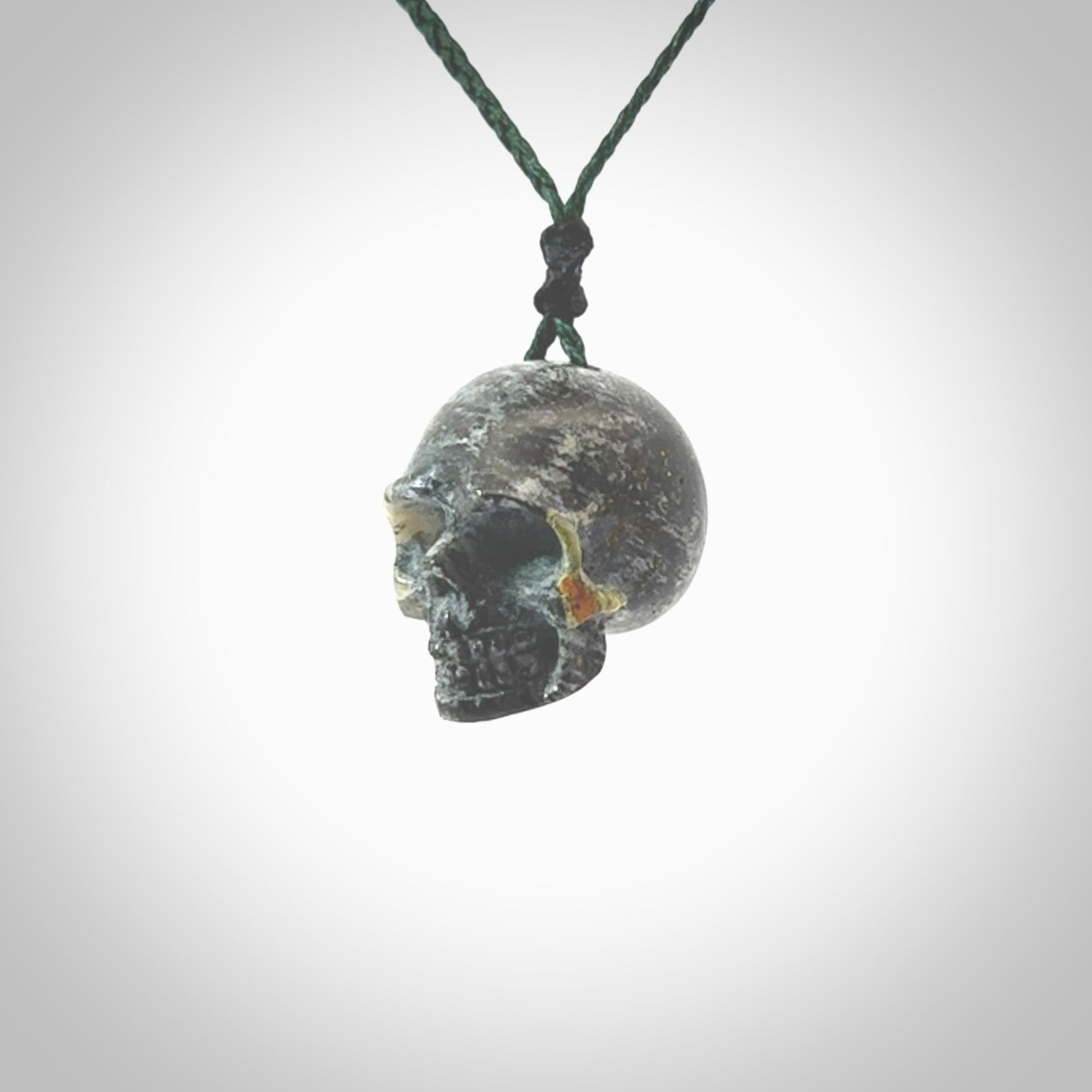 This picture shows a medium sized Bumblebee Jasper stone skull pendant that we have hand carved. It is polished to a soft shine and is a very striking piece. The cord is green colour and has a small black floret binding just above the pendant.