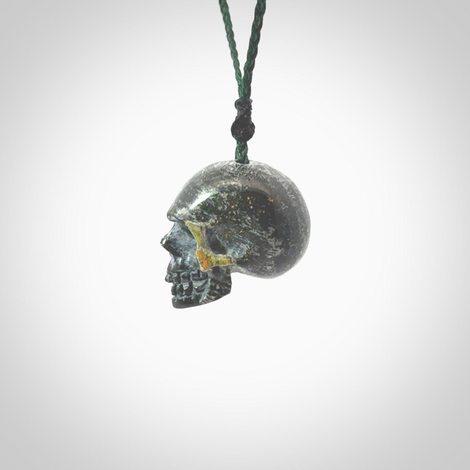 This picture shows a medium sized Bumblebee Jasper stone skull pendant that we have hand carved. It is polished to a soft shine and is a very striking piece. The cord is green colour and has a small black floret binding just above the pendant.