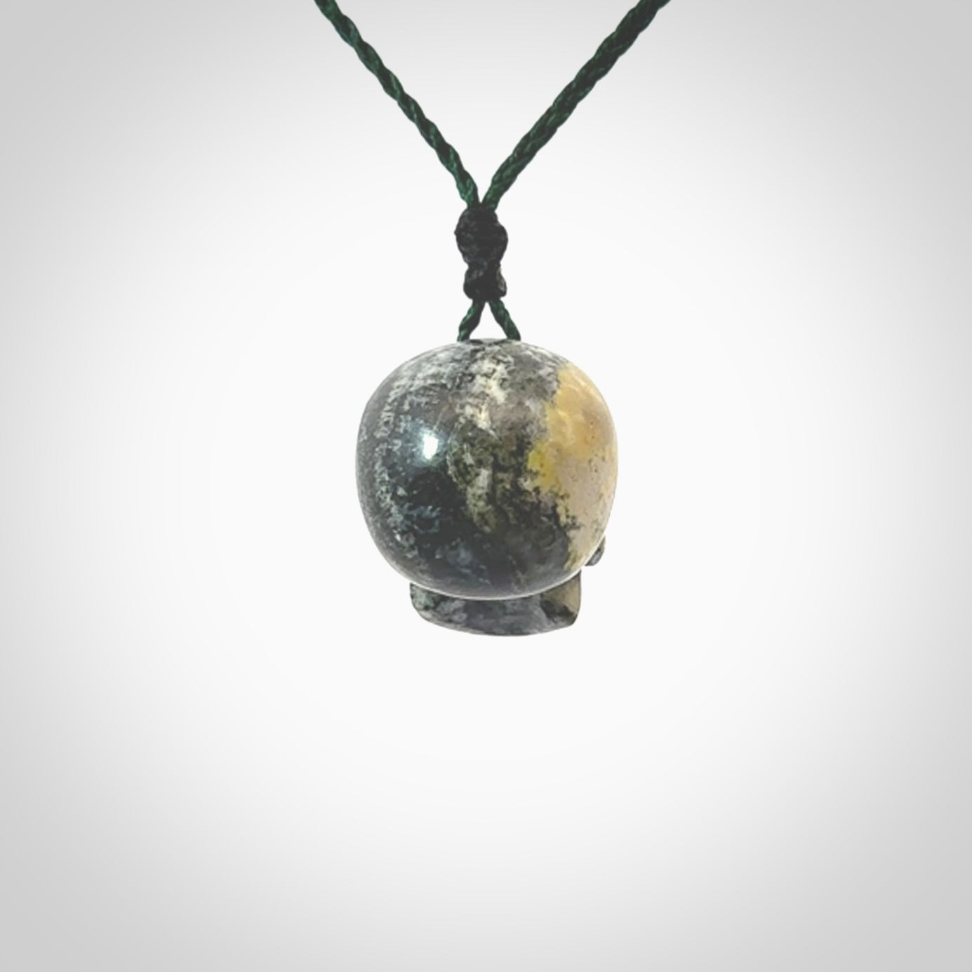 This picture shows a medium sized Bumblebee Jasper stone skull pendant that we have hand carved. It is polished to a soft shine and is a very striking piece. The cord is green colour and has a small black floret binding just above the pendant.