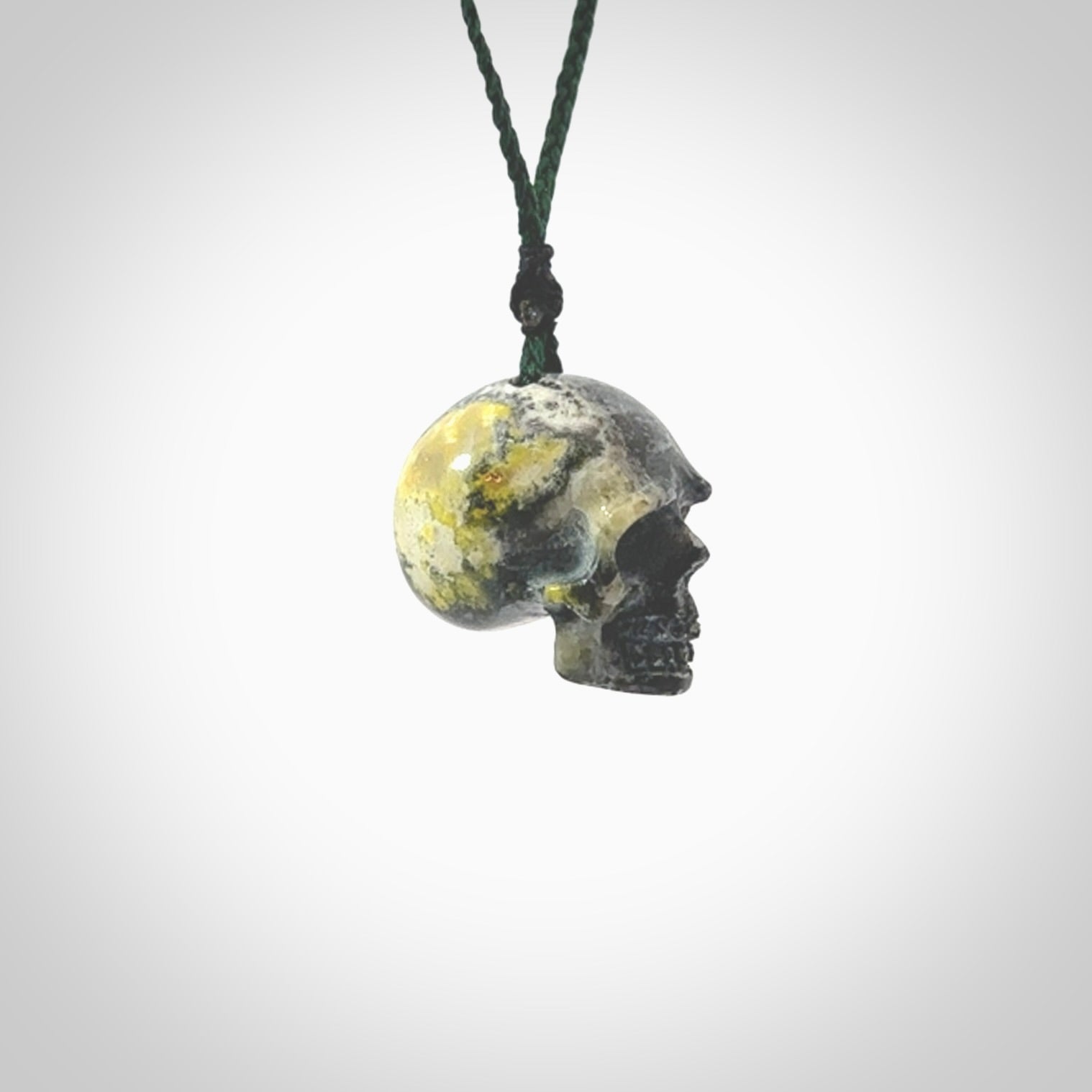 This picture shows a medium sized Bumblebee Jasper stone skull pendant that we have hand carved. It is polished to a soft shine and is a very striking piece. The cord is green colour and has a small black floret binding just above the pendant.