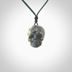 This picture shows a medium sized Bumblebee Jasper stone skull pendant that we have hand carved. It is polished to a soft shine and is a very striking piece. The cord is green colour and has a small black floret binding just above the pendant.