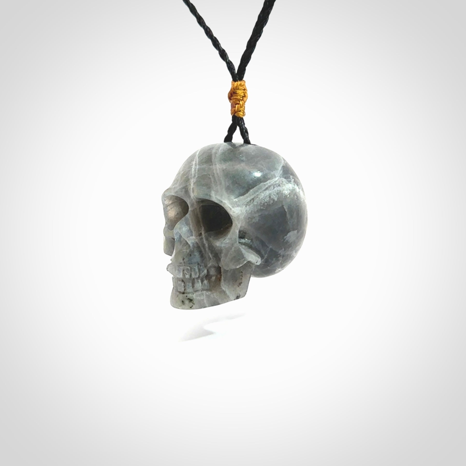 This picture shows a large sized Labradorite skull pendant that we have hand carved. It is polished to a soft shine and is a very striking piece. The cord is black and has a small gold floret binding just above the pendant.