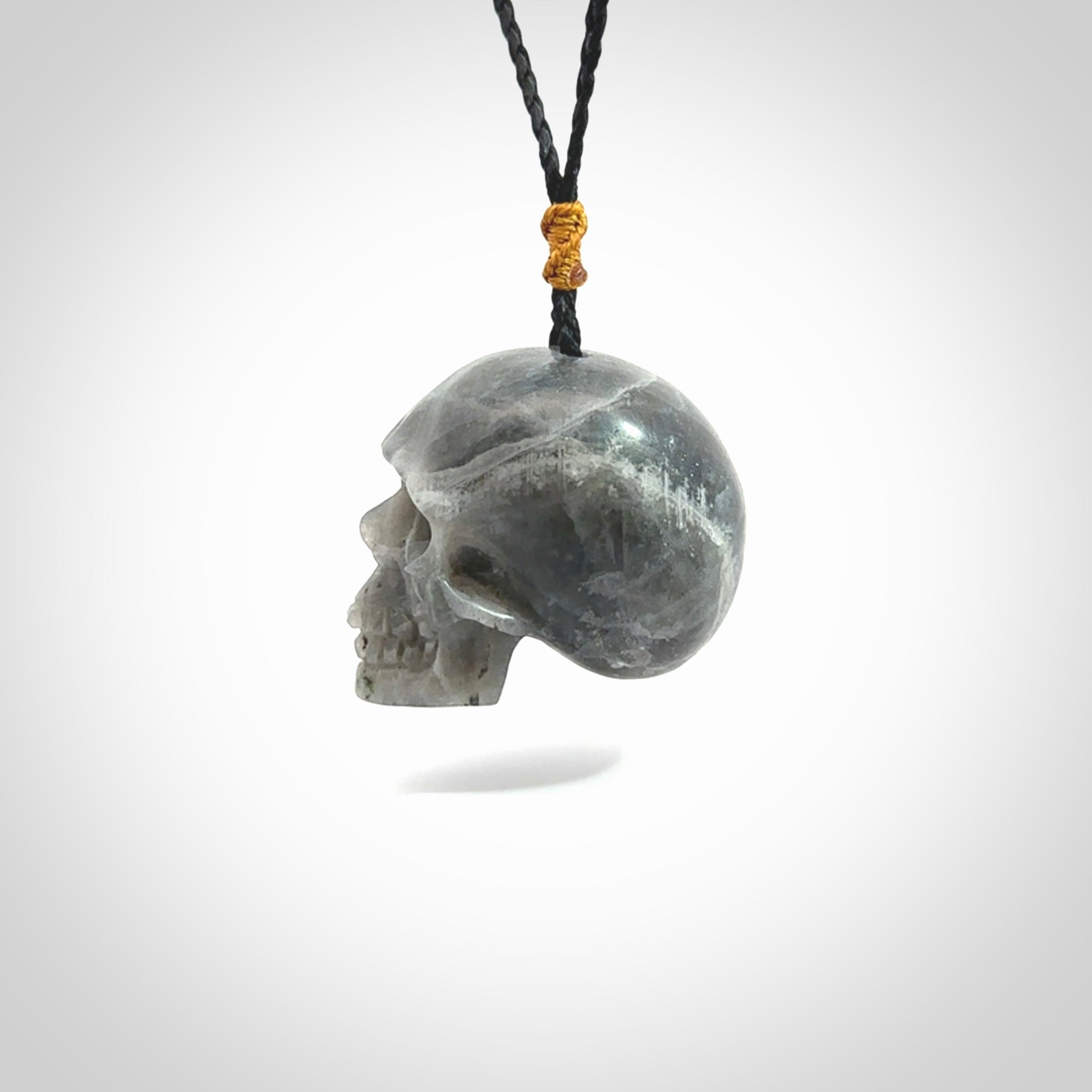 This picture shows a large sized Labradorite skull pendant that we have hand carved. It is polished to a soft shine and is a very striking piece. The cord is black and has a small gold floret binding just above the pendant.