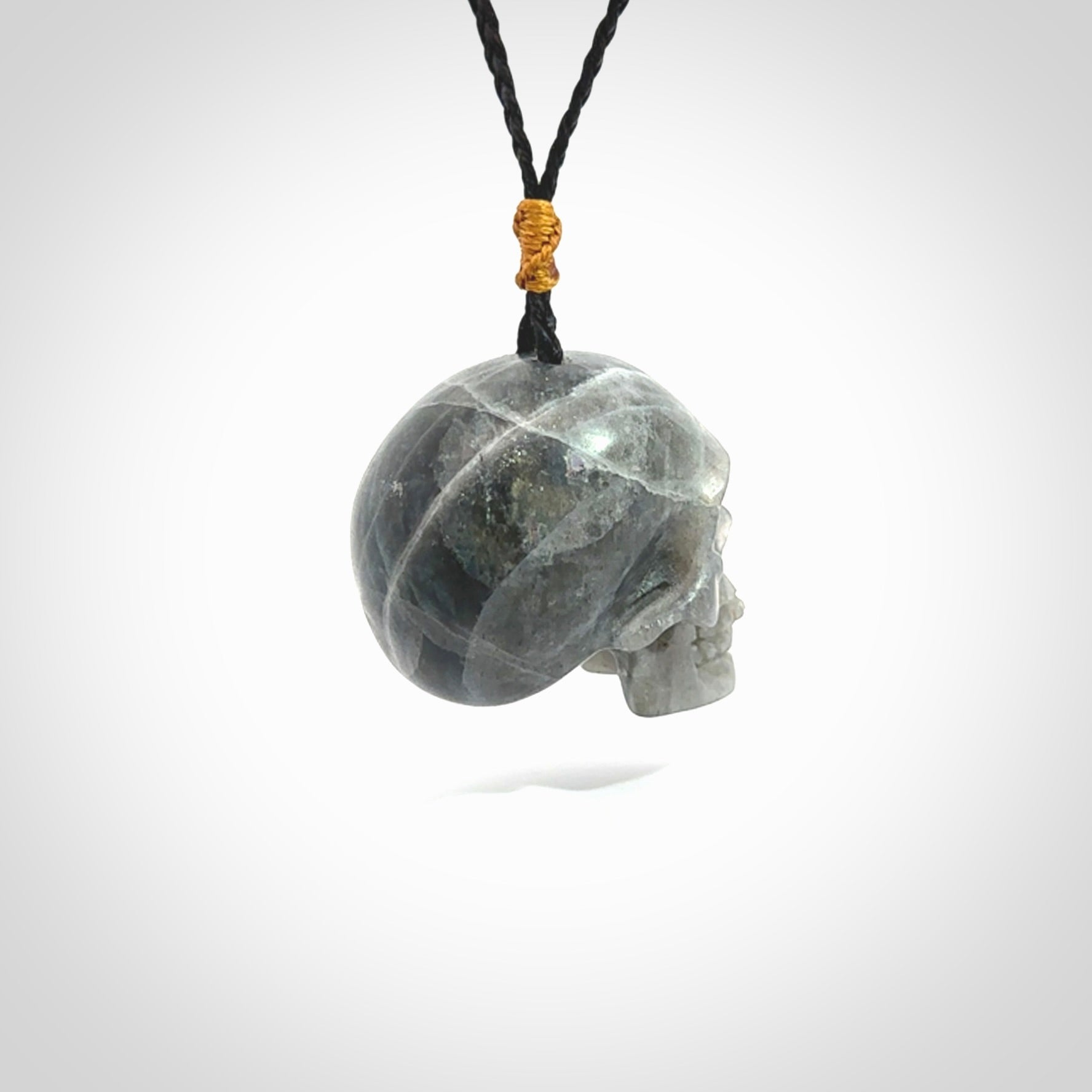 This picture shows a large sized Labradorite skull pendant that we have hand carved. It is polished to a soft shine and is a very striking piece. The cord is black and has a small gold floret binding just above the pendant.