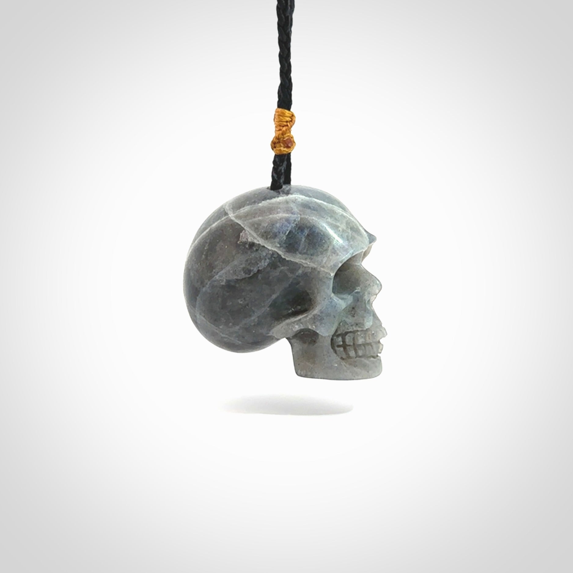 This picture shows a large sized Labradorite skull pendant that we have hand carved. It is polished to a soft shine and is a very striking piece. The cord is black and has a small gold floret binding just above the pendant.