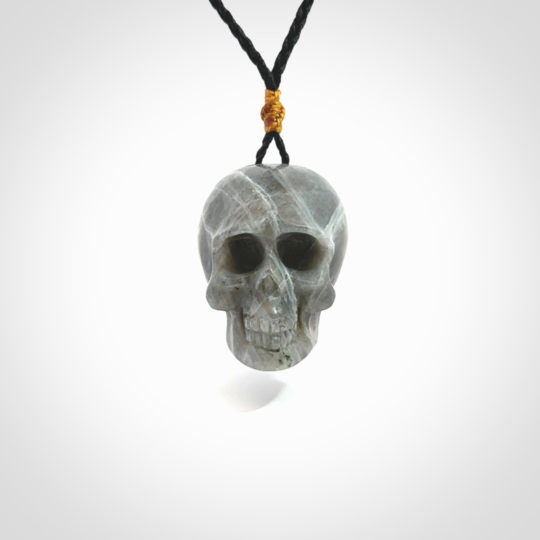 This picture shows a large sized Labradorite skull pendant that we have hand carved. It is polished to a soft shine and is a very striking piece. The cord is black and has a small gold floret binding just above the pendant.