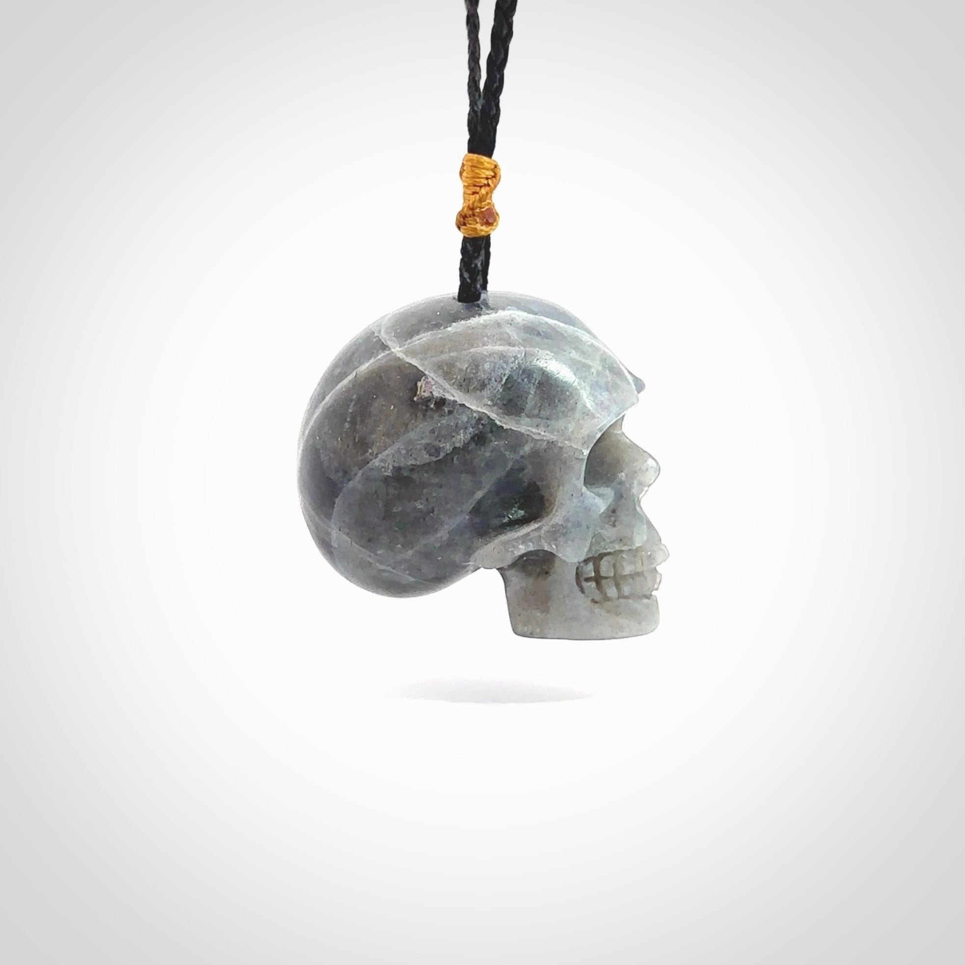 This picture shows a large sized Labradorite skull pendant that we have hand carved. It is polished to a soft shine and is a very striking piece. The cord is black and has a small gold floret binding just above the pendant.