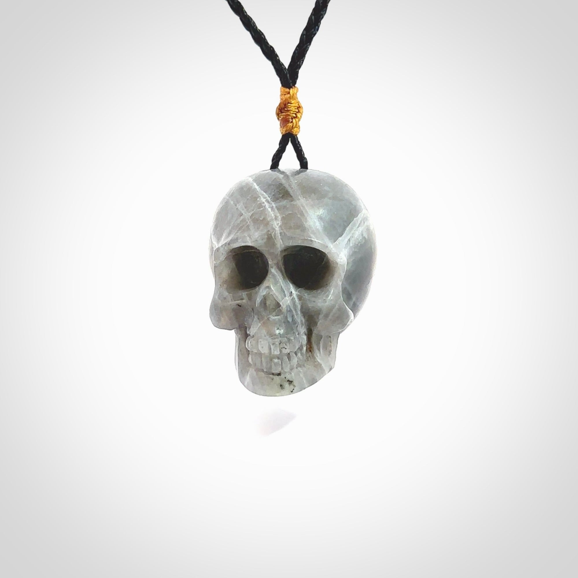 This picture shows a large sized Labradorite skull pendant that we have hand carved. It is polished to a soft shine and is a very striking piece. The cord is black and has a small gold floret binding just above the pendant.