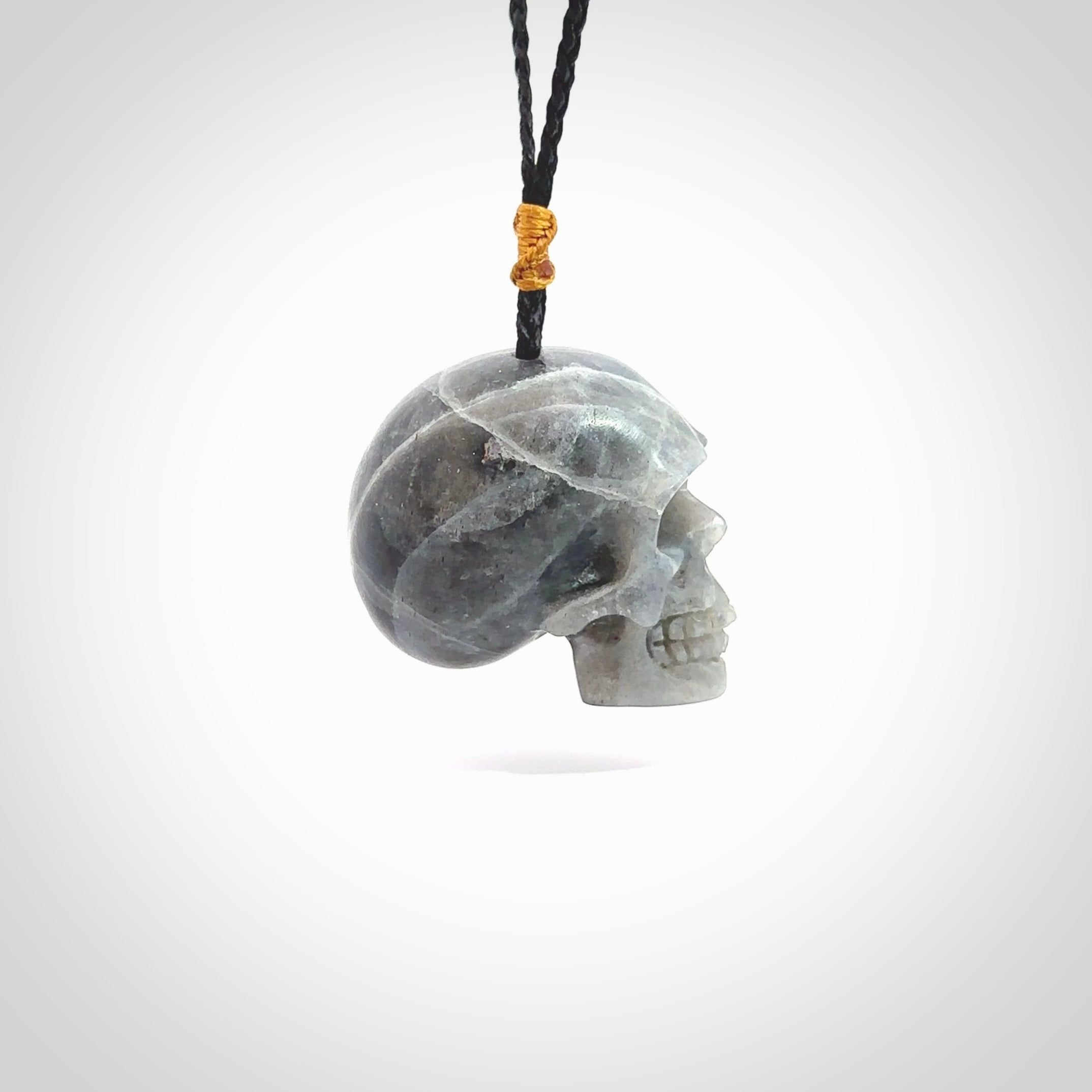 This picture shows a large sized Labradorite skull pendant that we have hand carved. It is polished to a soft shine and is a very striking piece. The cord is black and has a small gold floret binding just above the pendant.