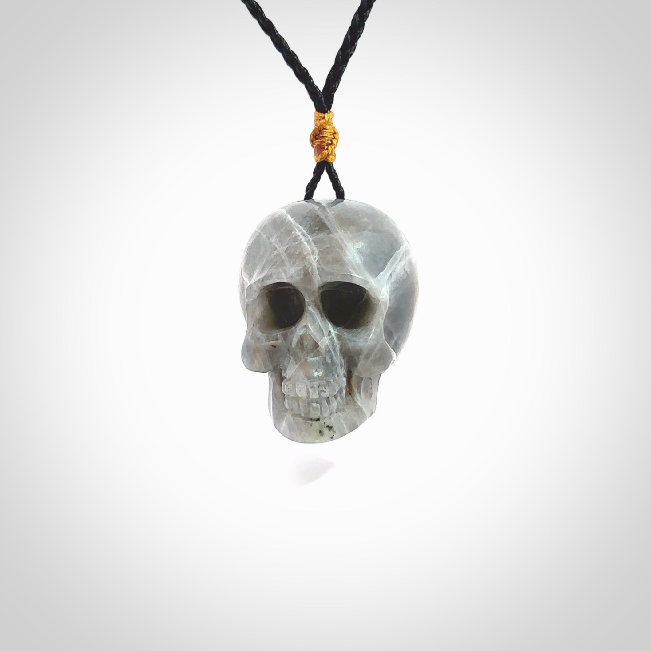 This picture shows a large sized Labradorite skull pendant that we have hand carved. It is polished to a soft shine and is a very striking piece. The cord is black and has a small gold floret binding just above the pendant.