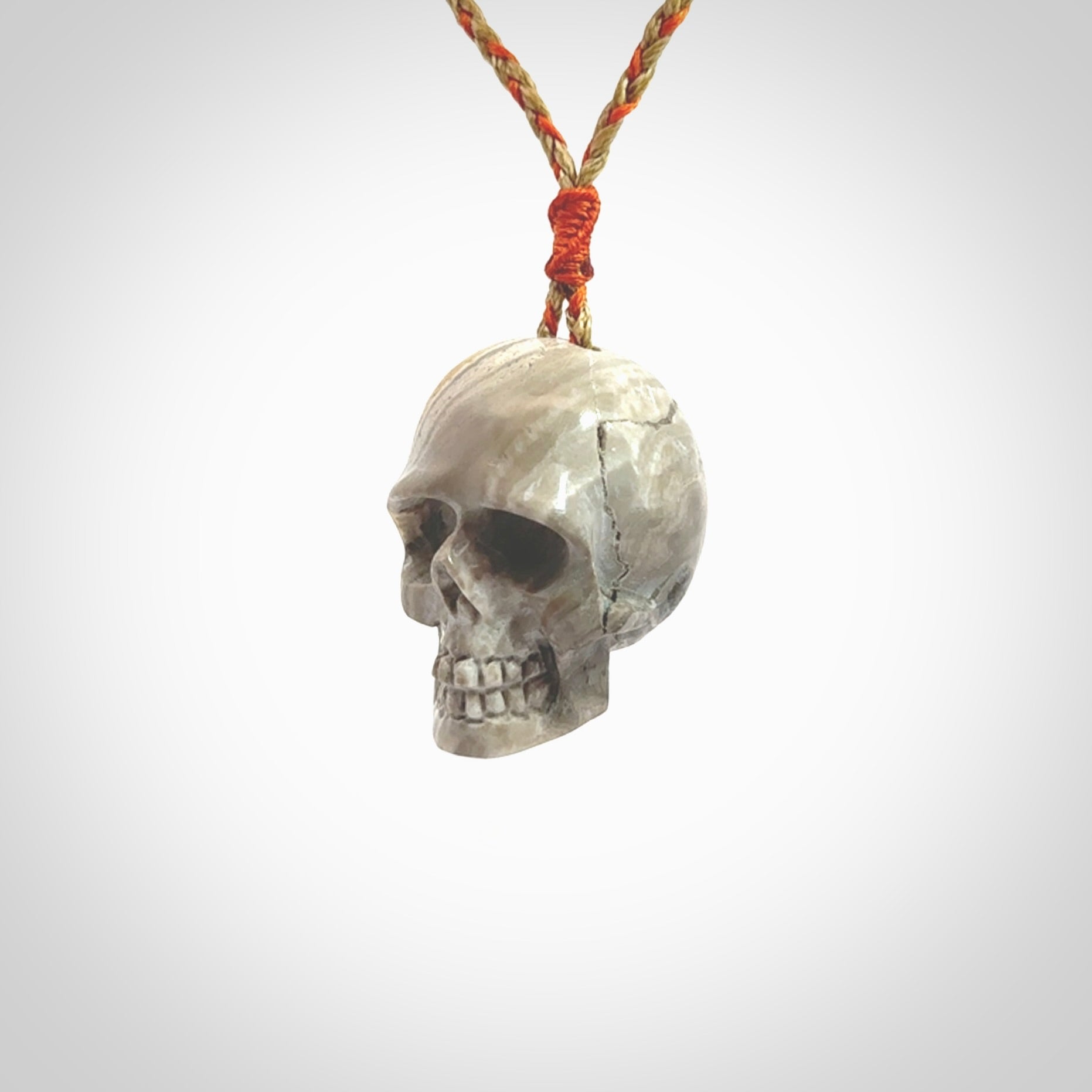 This picture shows a large sized Bumblebee Jasper stone skull pendant that we have hand carved. It is polished to a soft shine and is a very striking piece. The cord is a orange and tan colour and has a small orange floret binding just above the pendant.