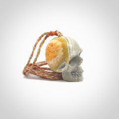 This picture shows a large sized Bumblebee Jasper stone skull pendant that we have hand carved. It is polished to a soft shine and is a very striking piece. The cord is a orange and tan colour and has a small orange floret binding just above the pendant.